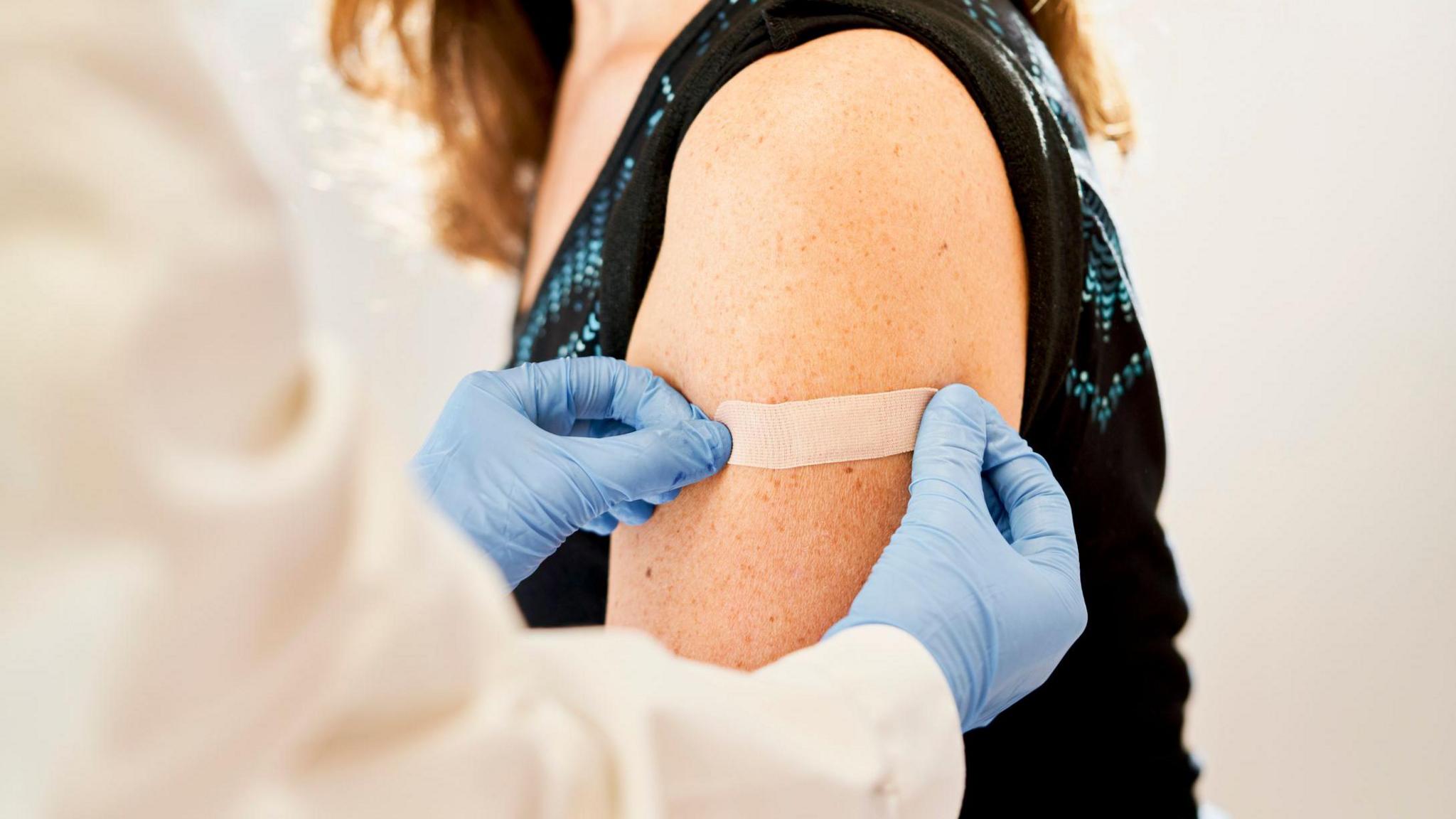 Doctor applying band-aid to a patient, whose face cannot be seen, after receiving the third dose of vaccine for immunization - stock photo