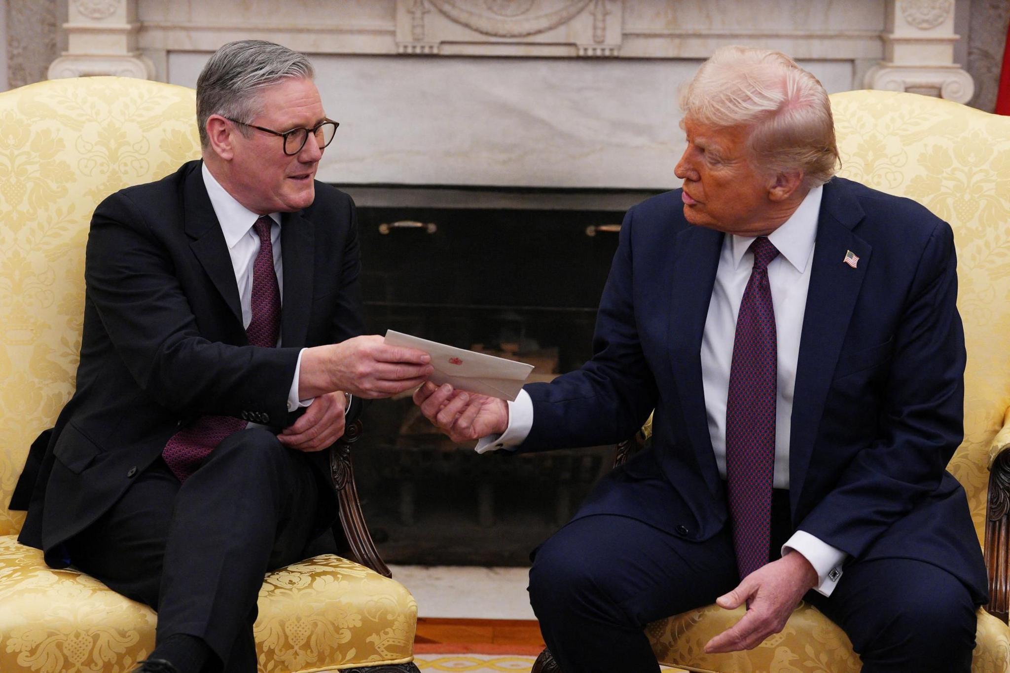 Sir Keir Starmer hands an envelope to Donald Trump, who is talking. They are sitting in yellow chairs and both wearing suits.