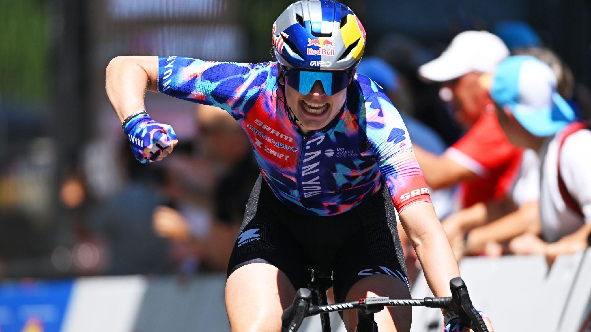 Zoe Backstedt with one hand on the handlebars punches the air with her right fist as she crosses the line