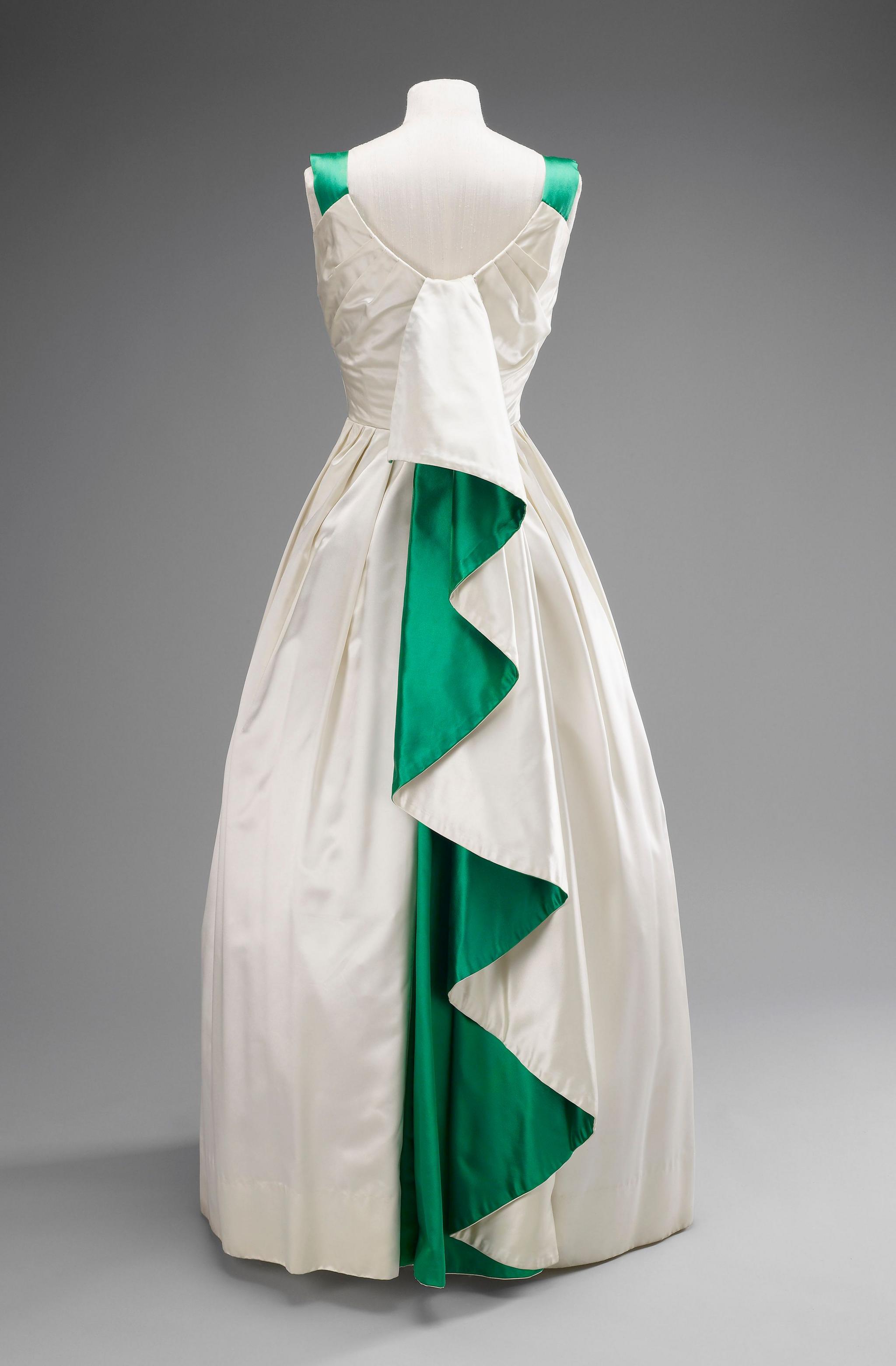 the back of a strapped dress which is coloured white with a bright green pleat draped down the back and green accents on the top of the straps