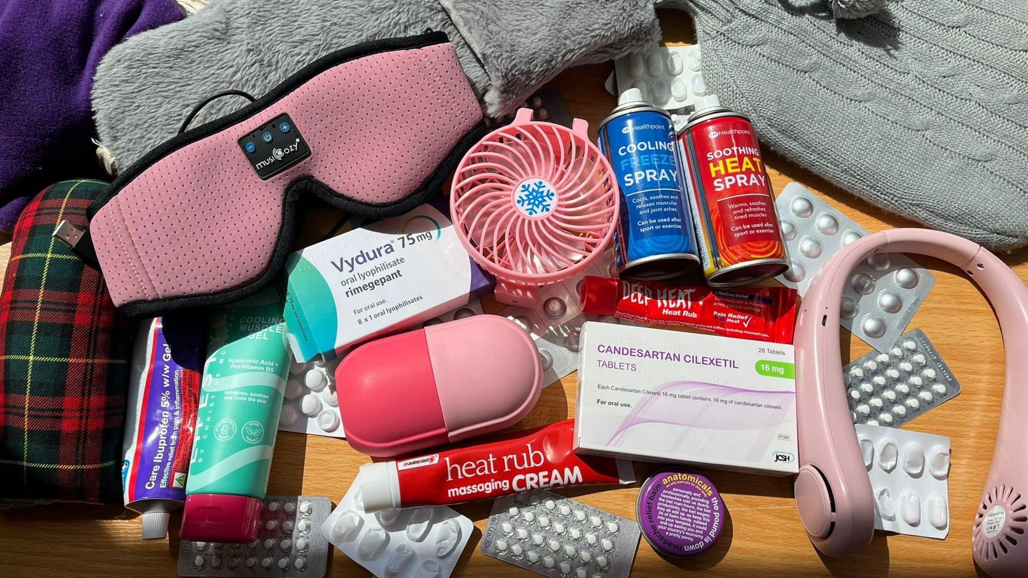 Picture of Kayleigh Webster's migraine tool kit - medication boxes, eye mask, deep heat, headphones, a fan and hot water bottles
