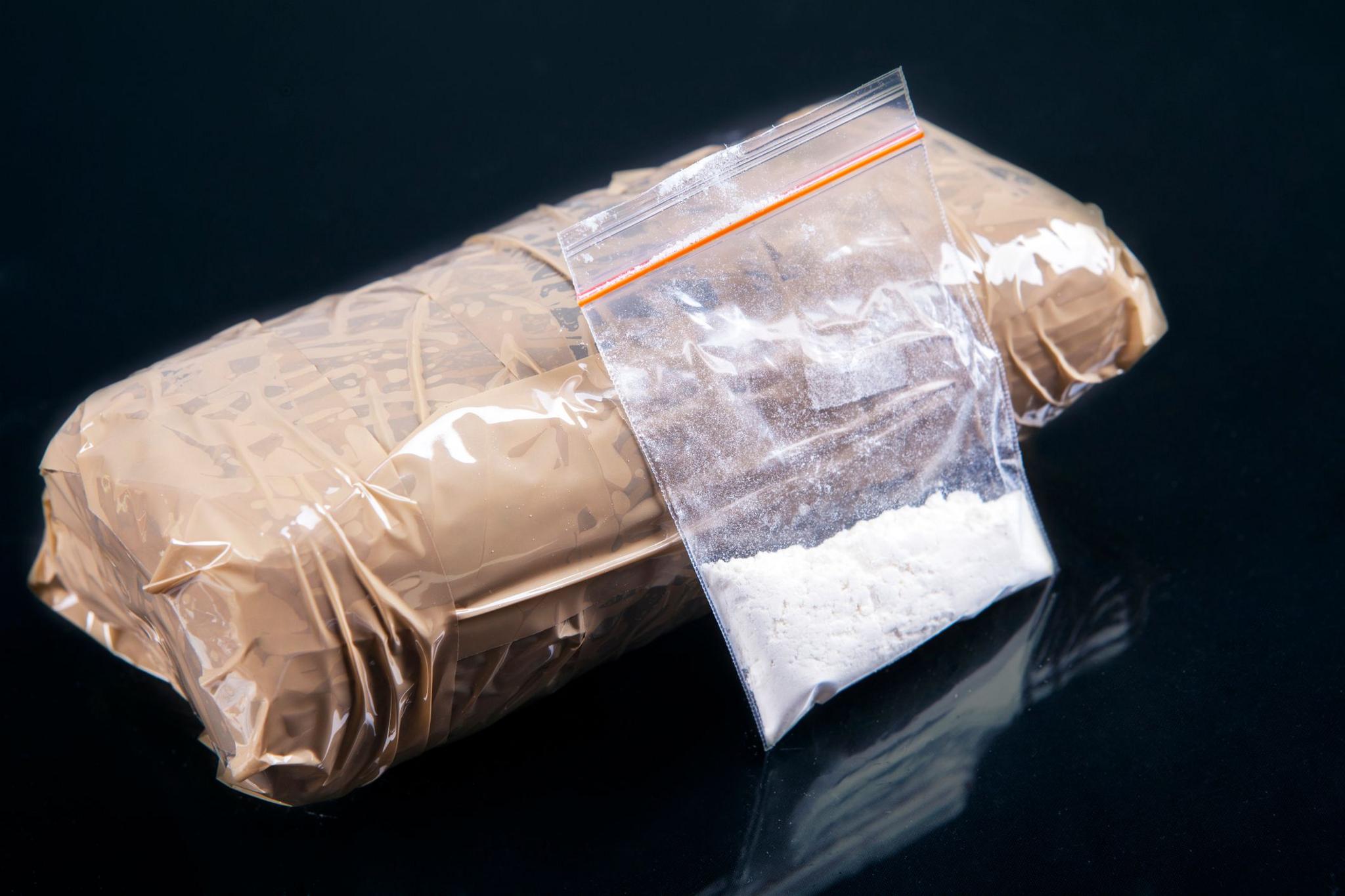 A small plastic bag containing a white powder next to a package wrapped in brown parcel tape.