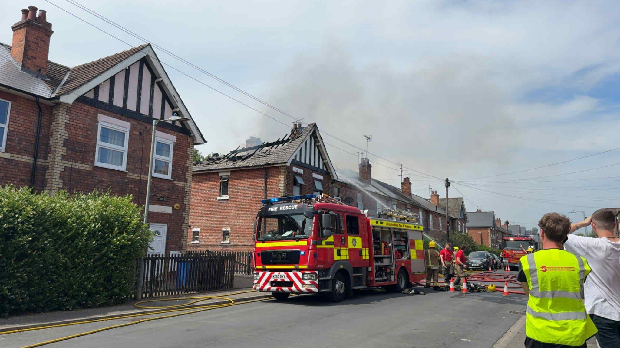 Fire engines outside a row of terraced houses. Smoke billows from above the houses.