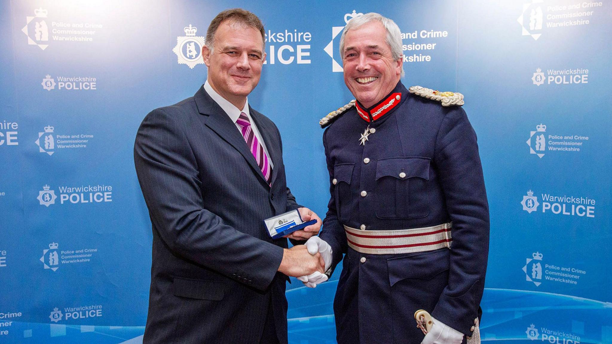 A white man in a blue suit shaking hands with a senior officer