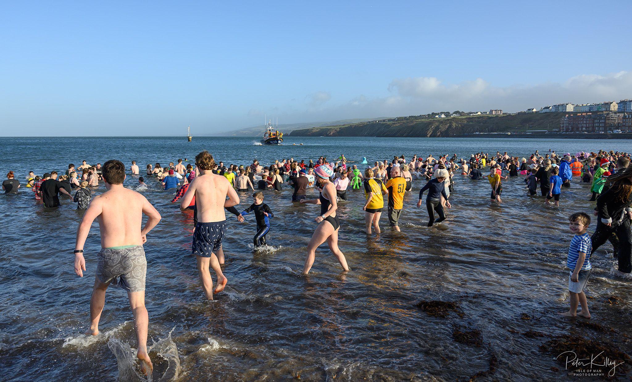 Hundreds of people standing in the sea at Peel, there is an RNLI Lifeboat in the background.