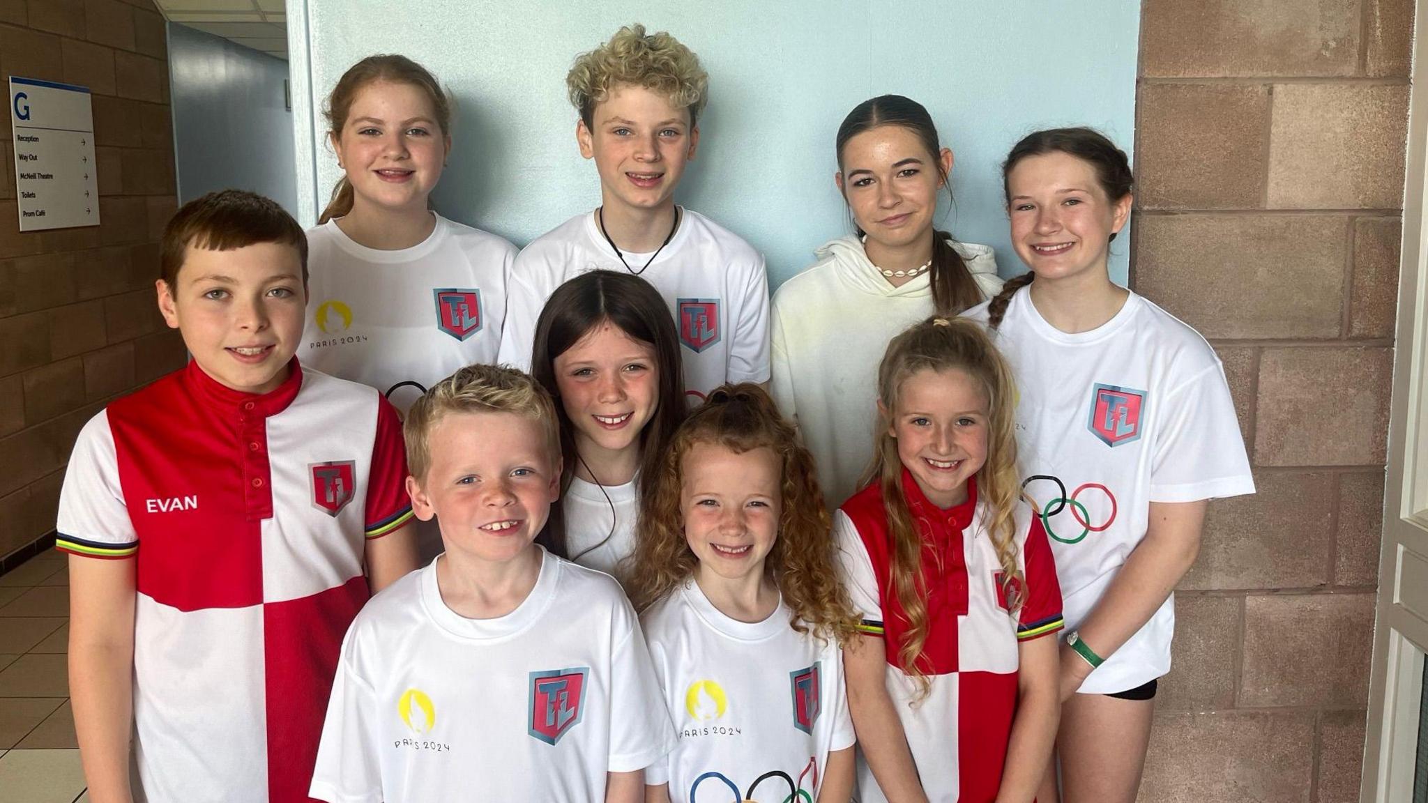 Nine children standing together wearing white t-shirts and red and white chequered polo shirts