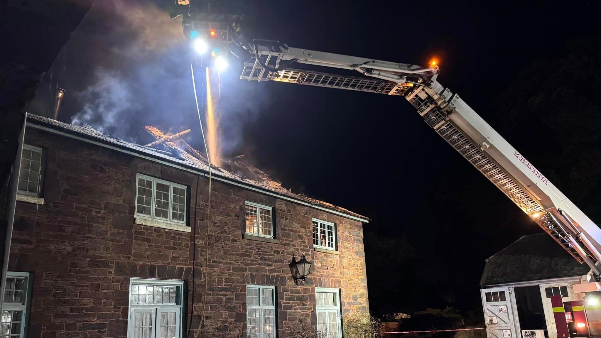 A picture of the fire service tackling the fire from above on an aerial ladder. The fire seems to be put out with only smoke coming from the roof