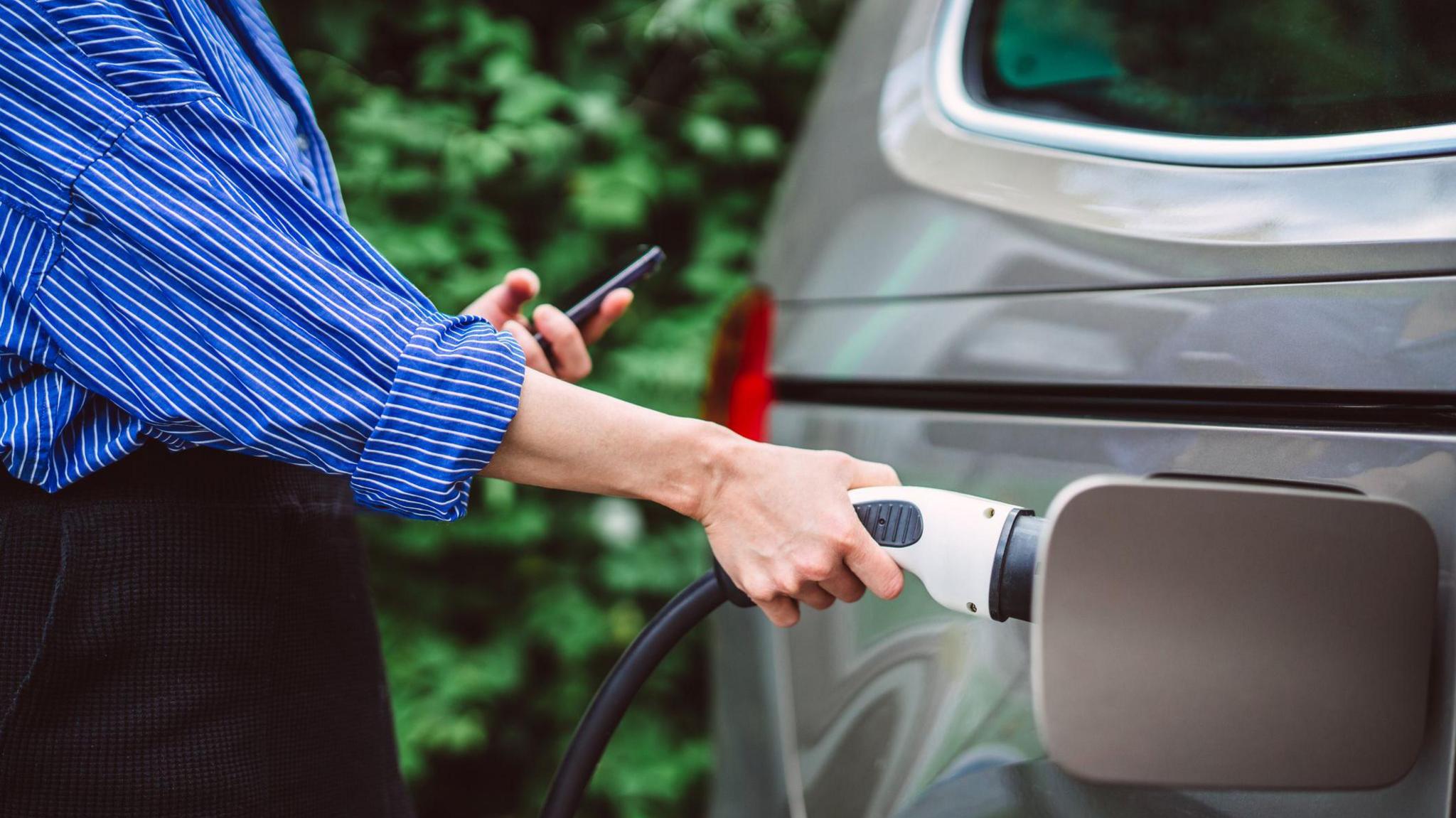 A close-up of a young woman charging her electric car.