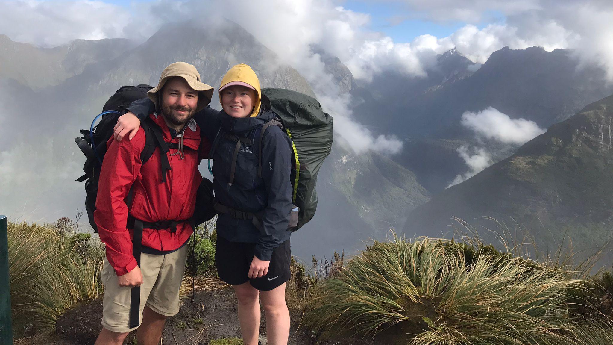 A young couple poses while hiking up a picture-esque mountain, covered in cloud