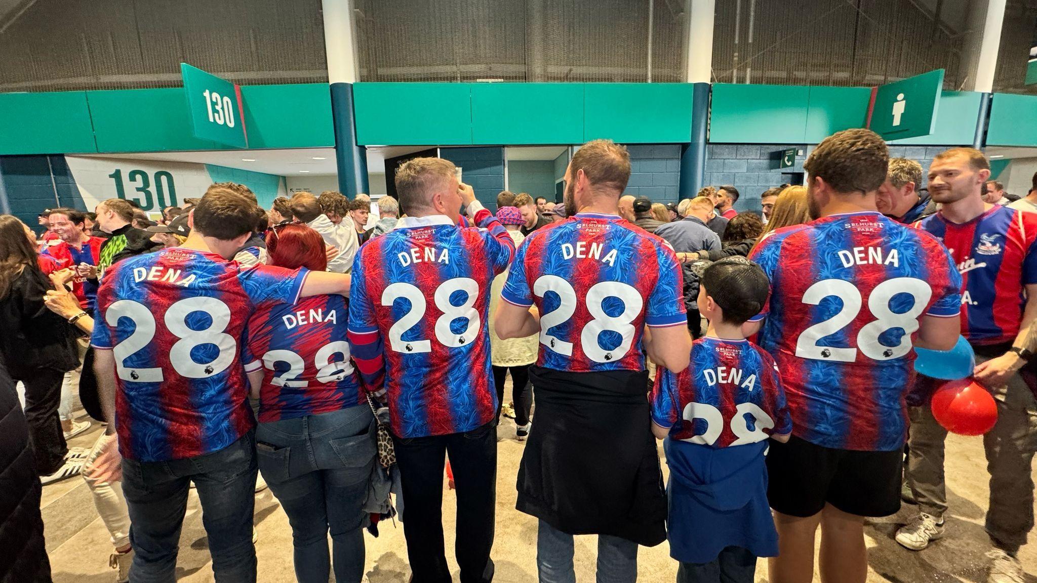 Family and friends of Crystal Palace fan Dena Collins pose with their back to the camera showing them all wearing 'Dena 28' on their shirts