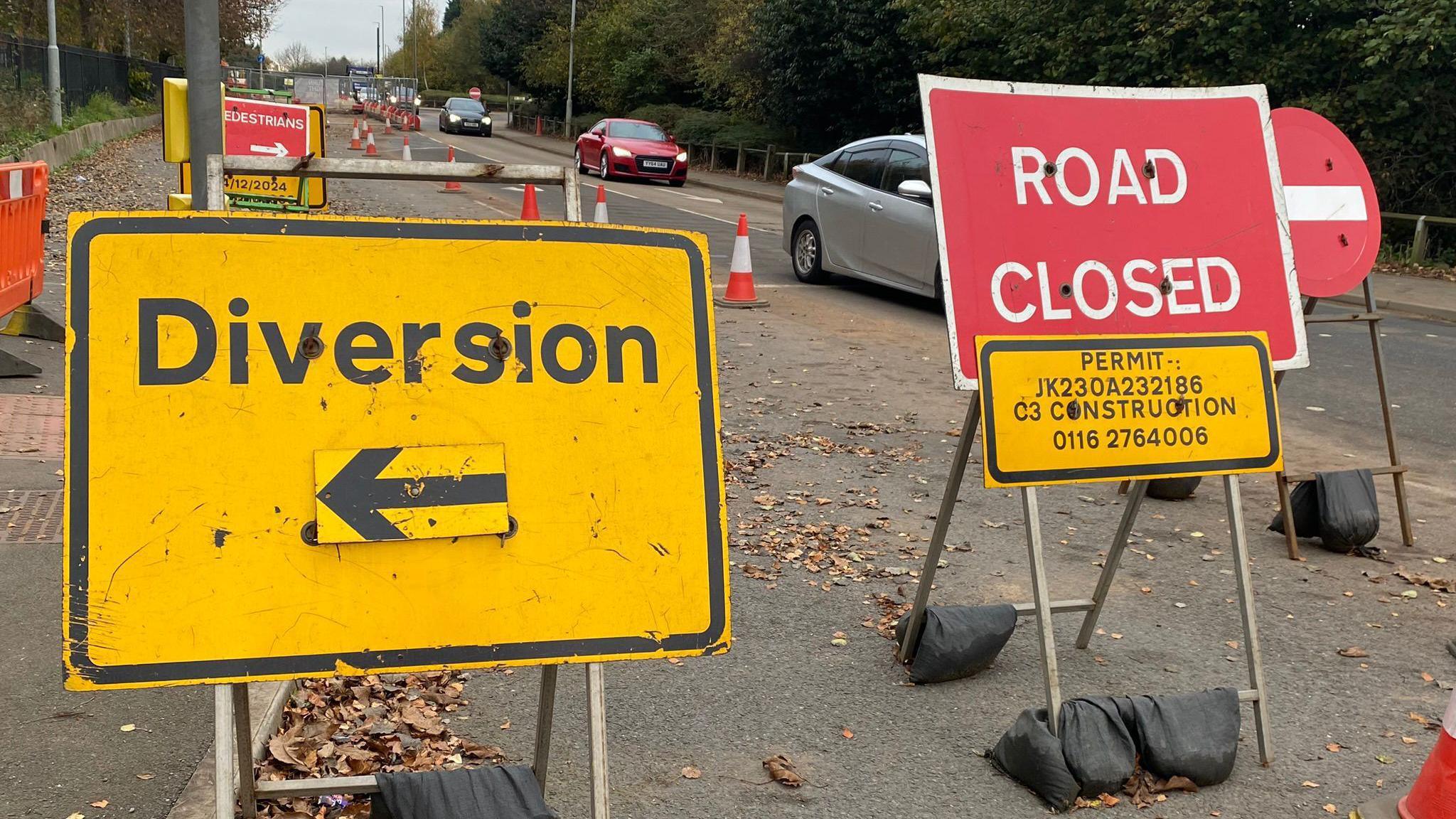 A busy road junction with an area coned off and several road signs saying Diversion, Road Closed and Pedestrians