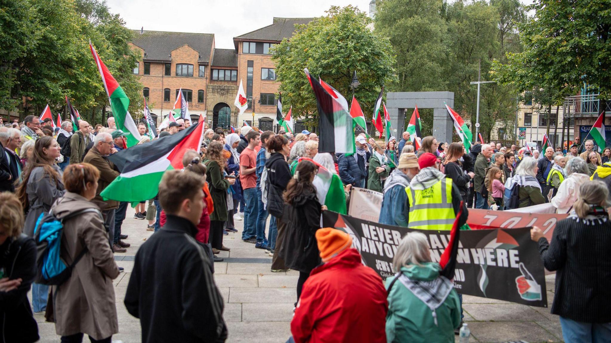 Crowds of protester in Writers' Square in Belfast city centre. Many of them are holding Palestinian flags and walking behind large banners
