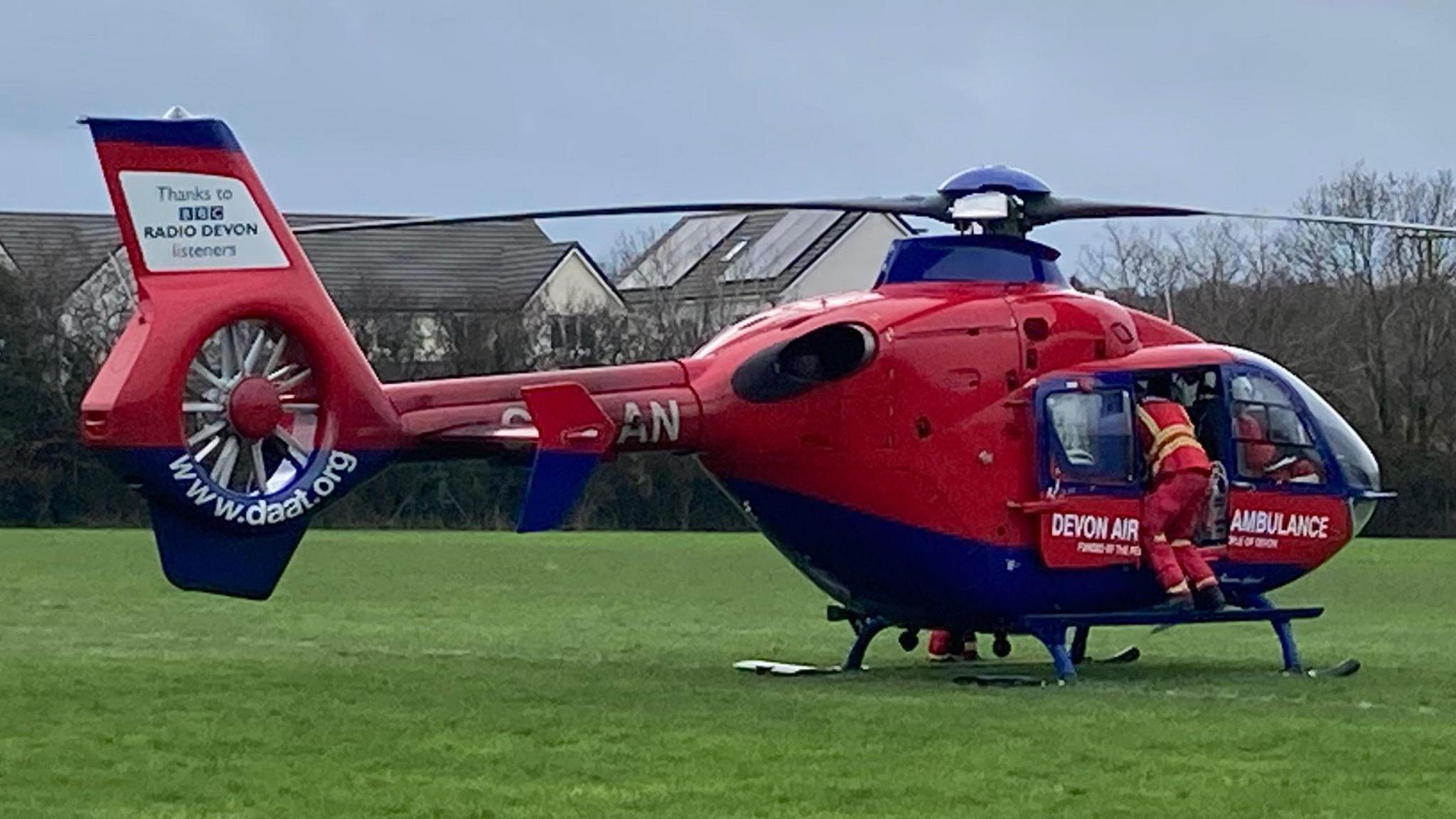 A red and blue air ambulance on a green grass field. 