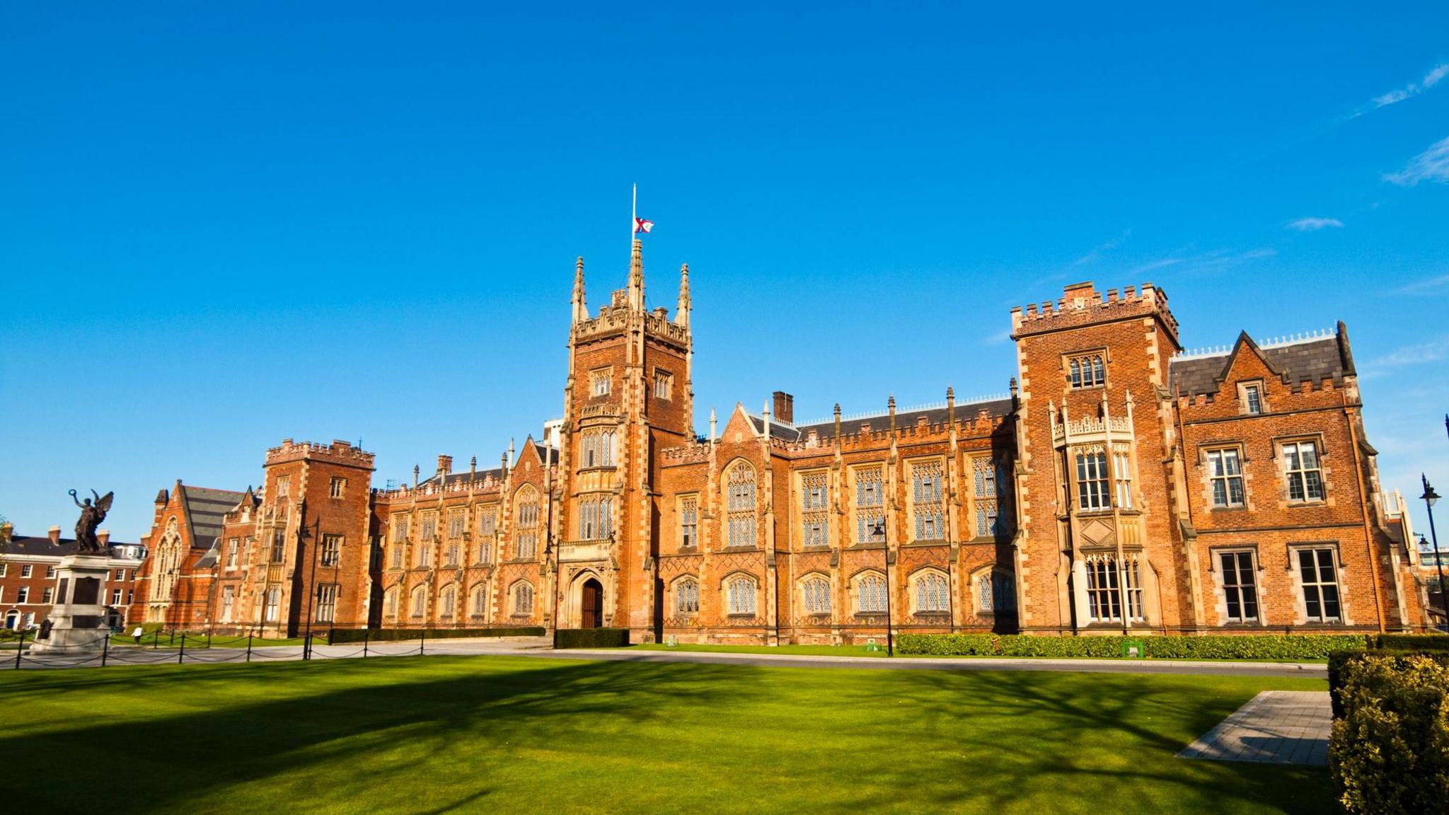 The exterior of Queen's University Belfast's red brick Lanyon Building, with a blue sky in the background and a green lawn at the front.