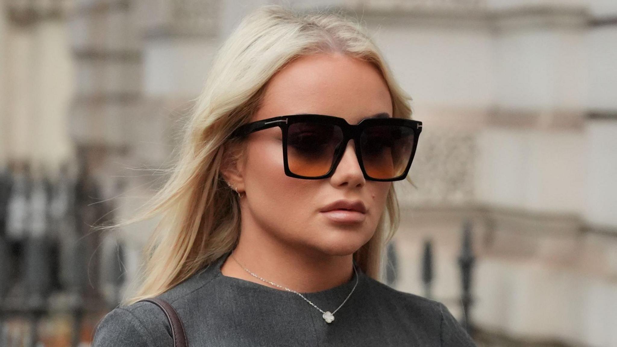 Victoria Thomas Bowen arriving at court. She has long blonde hair and is wearing black sunglasses, a silver necklace and a grey dress.