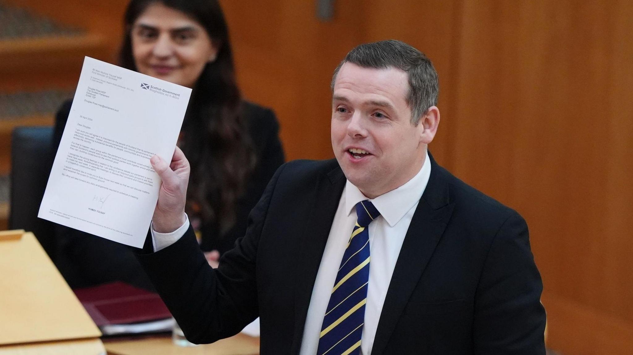 Douglas Ross addressing MSPs in the Scottish Parliament chamber. He is holding up a letter on Scottish government paper and speaking. 