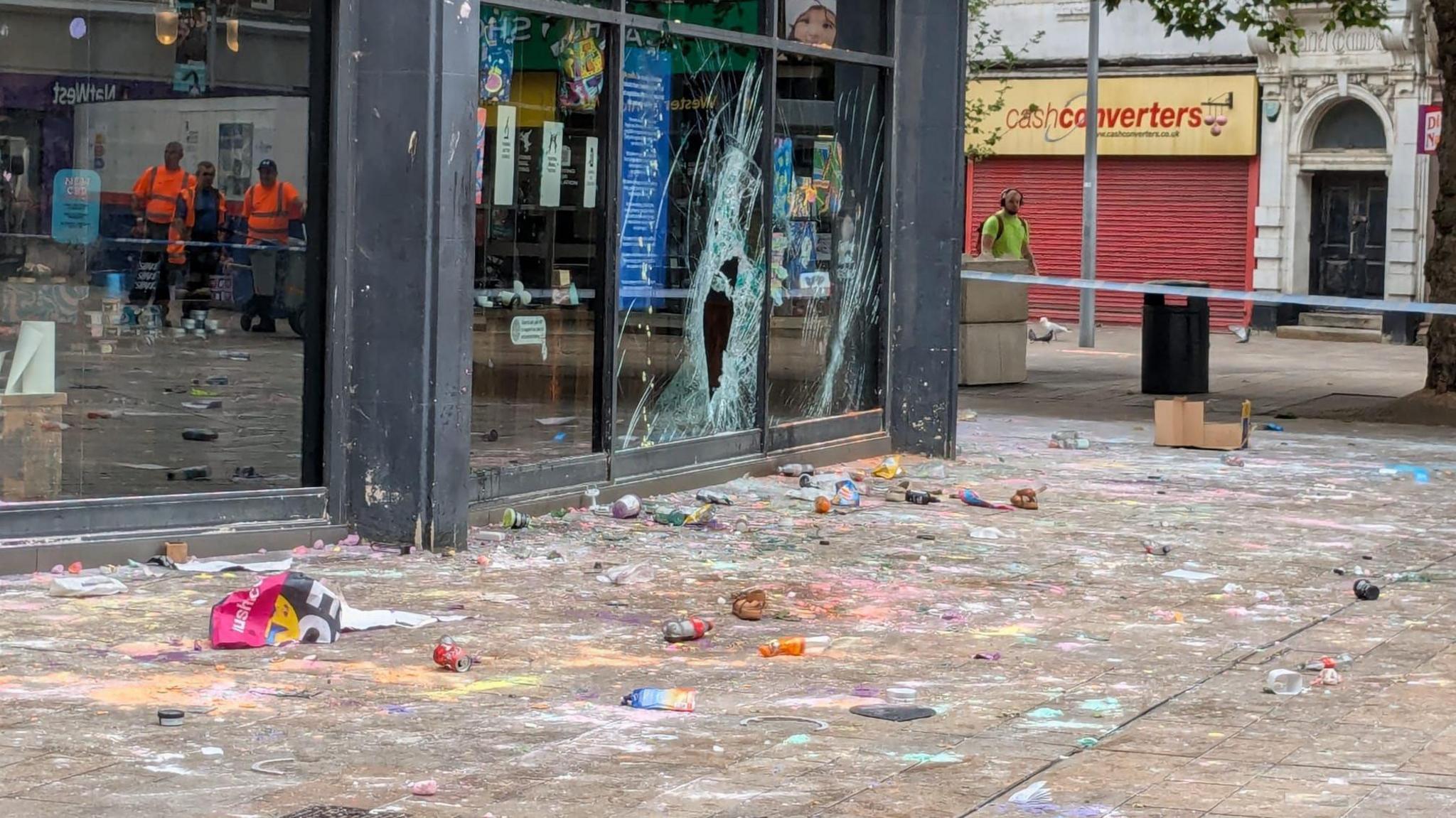 Rubbish and filth strewn all across the ground in front of a shop with a broken window