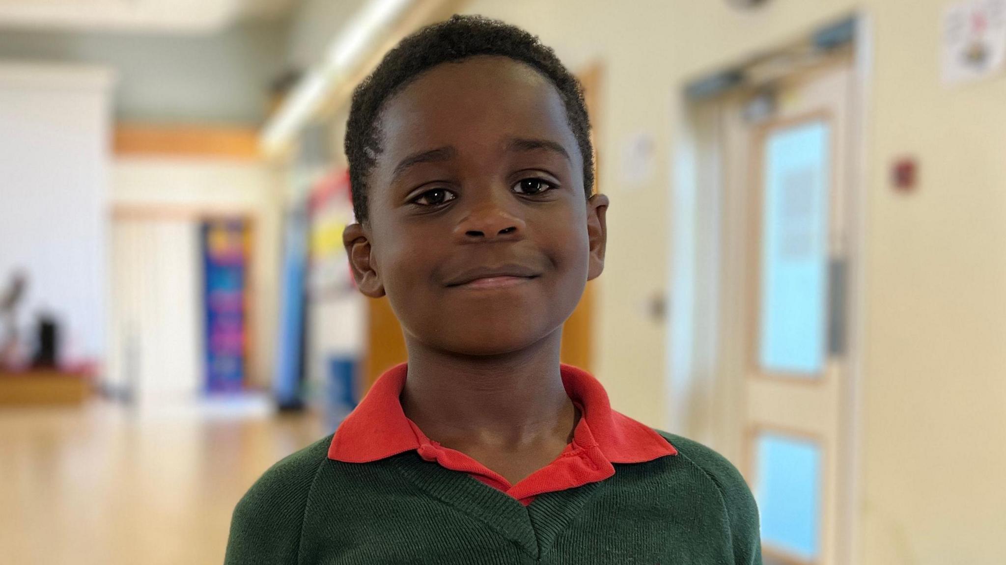 A boy in a green jumper and red polo shirt smiling at the camera