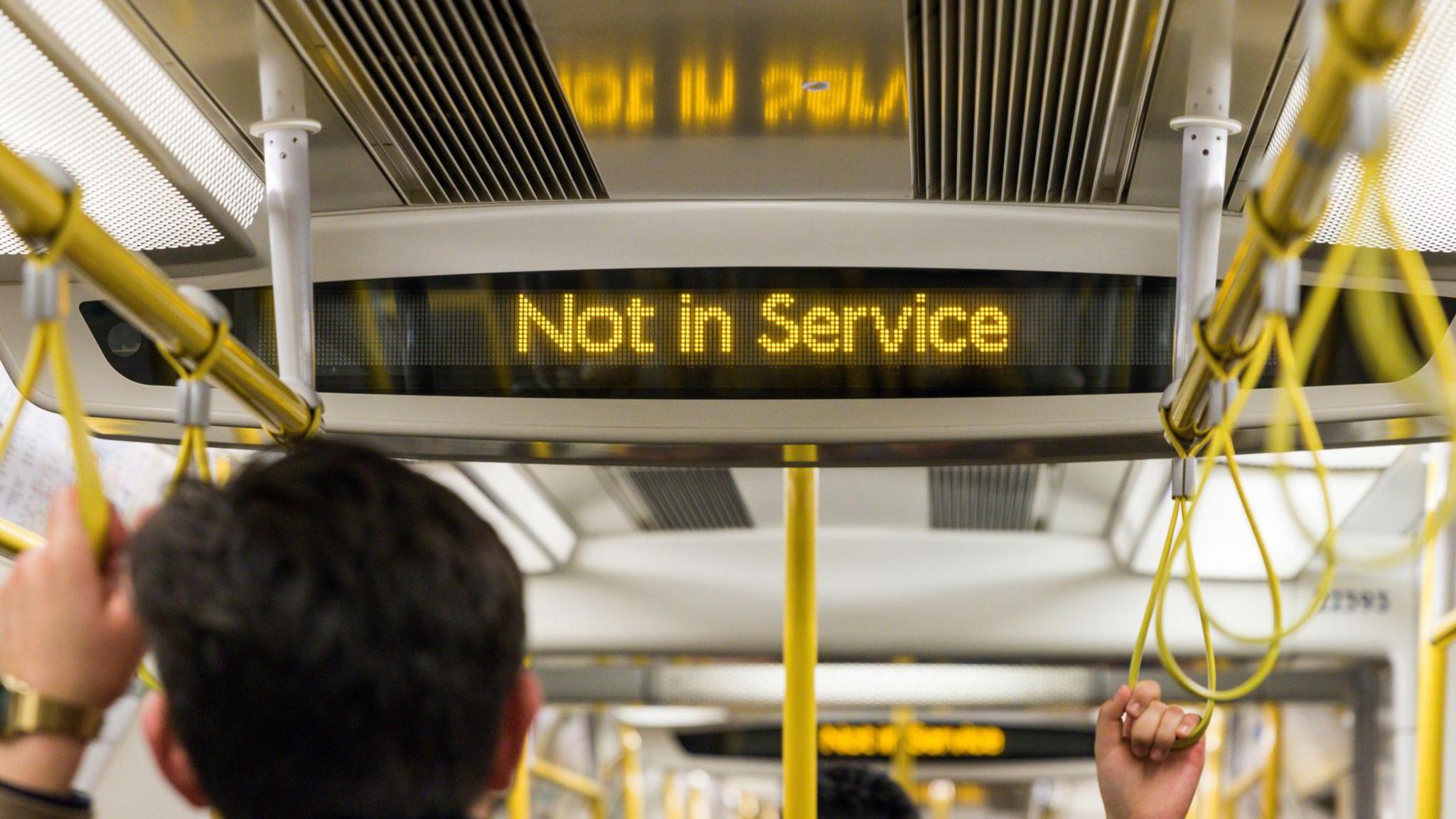 A "Not in Service" LED sign on London Underground train. A man is pictured holding onto a train handle