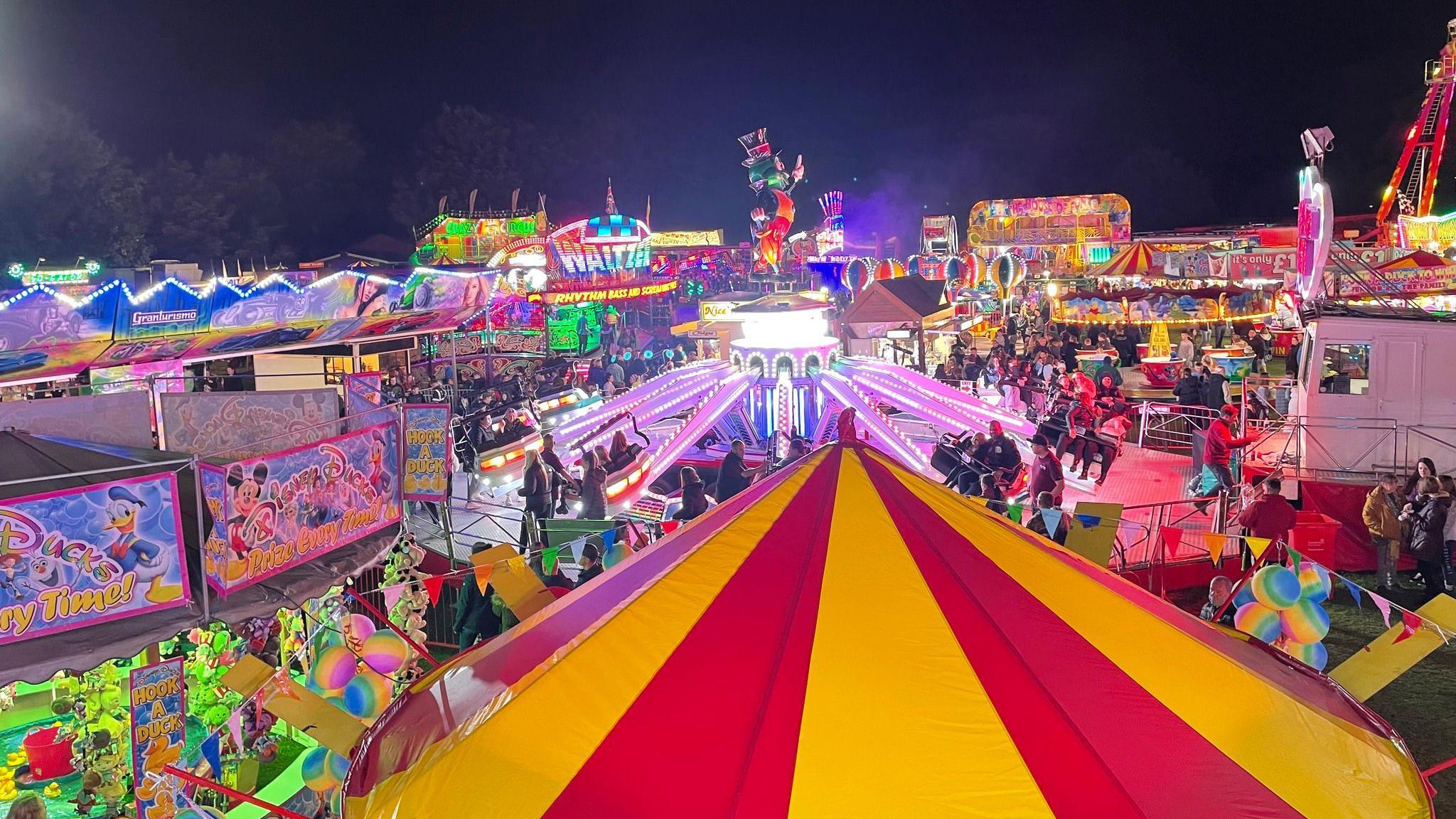 Fairground rides, including a waltzer, illuminated at night.
