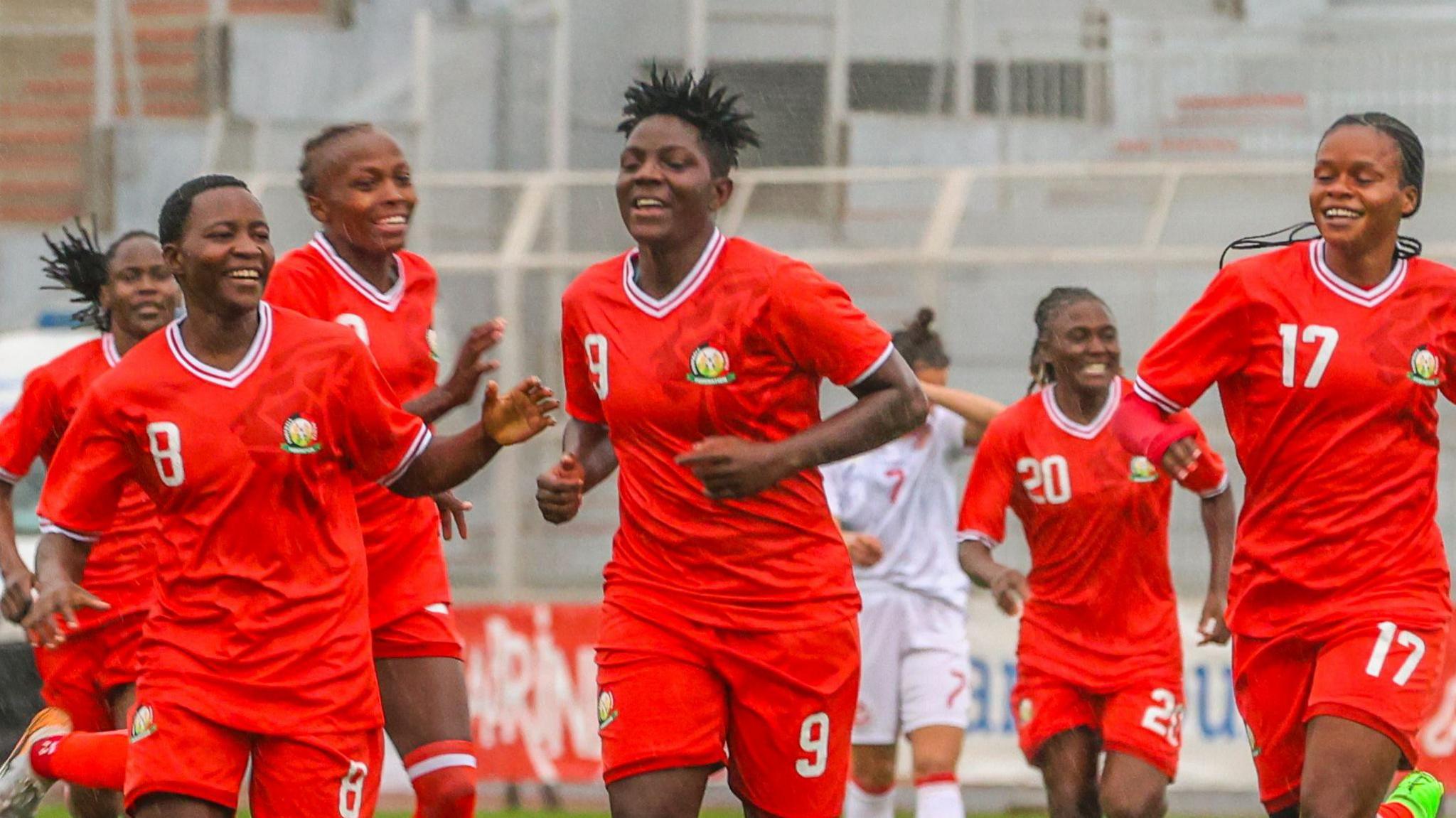 Six Kenya women's players wearing a red strip celebrate a goal during a football match against Tunisia