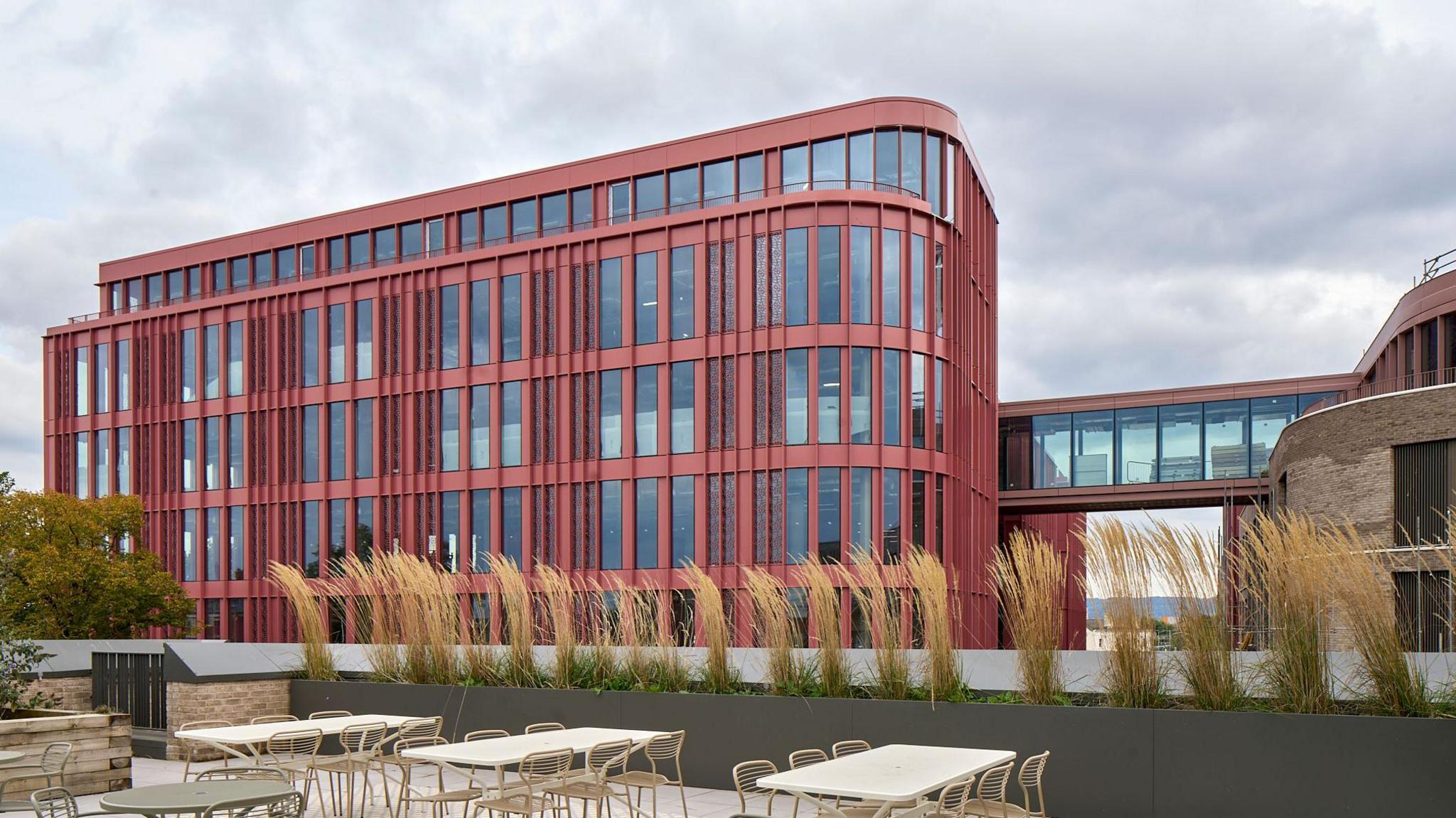 The exterior of the Forum building in Gloucester. The building has a red facade and chairs and tables outside.