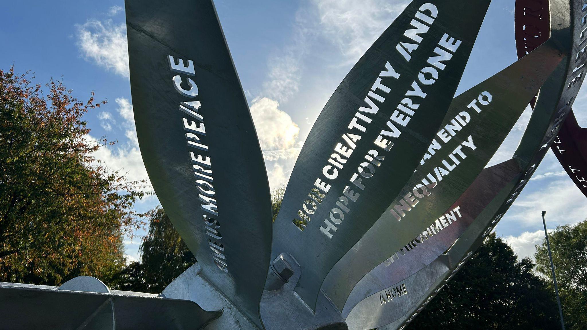 Words laser cut into the blades of a large silver wheel which is part of the sculpture