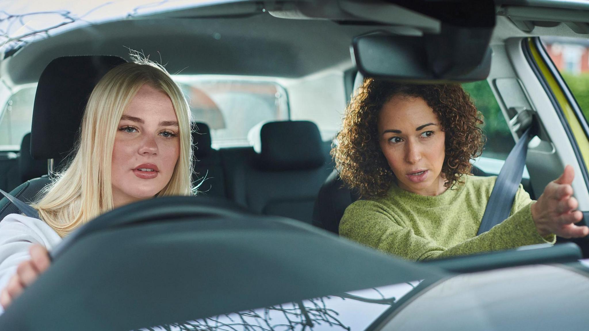 A stock image of a blonde learner driver listening to guidance from an instructor