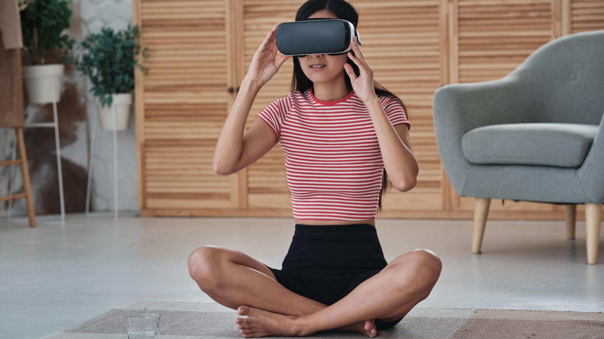 Woman in a stripy top sitting on a yoga mat and wearing a VR headset