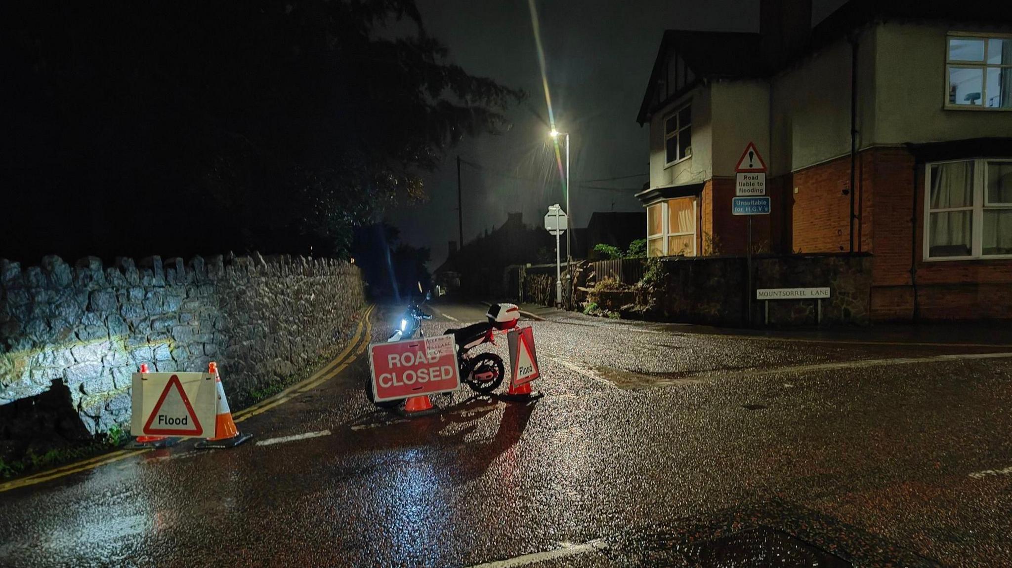 A road is blocked by traffic cones and signs warning of flooding.