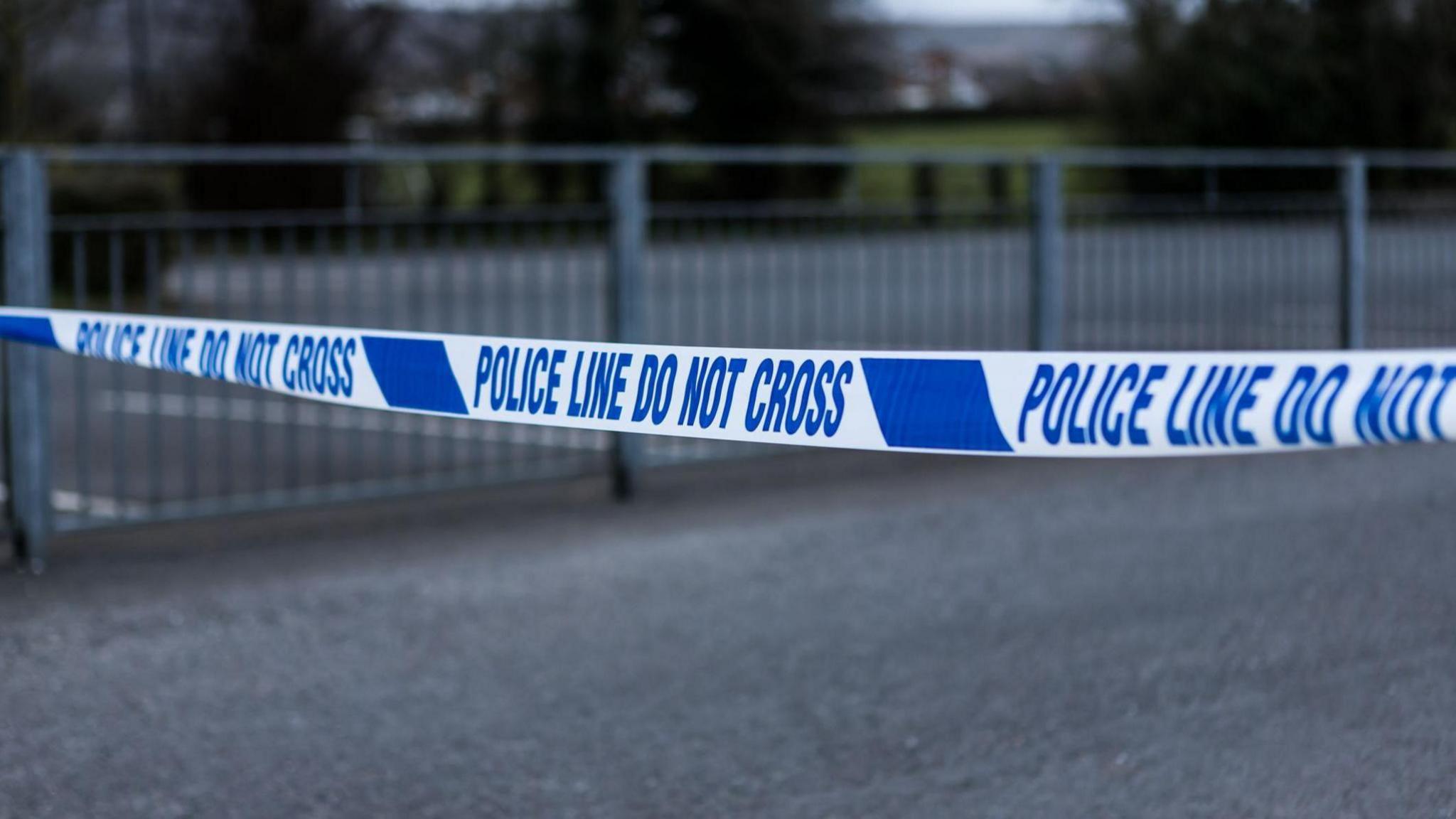 Blue and white police tape with a grey fence in the background.