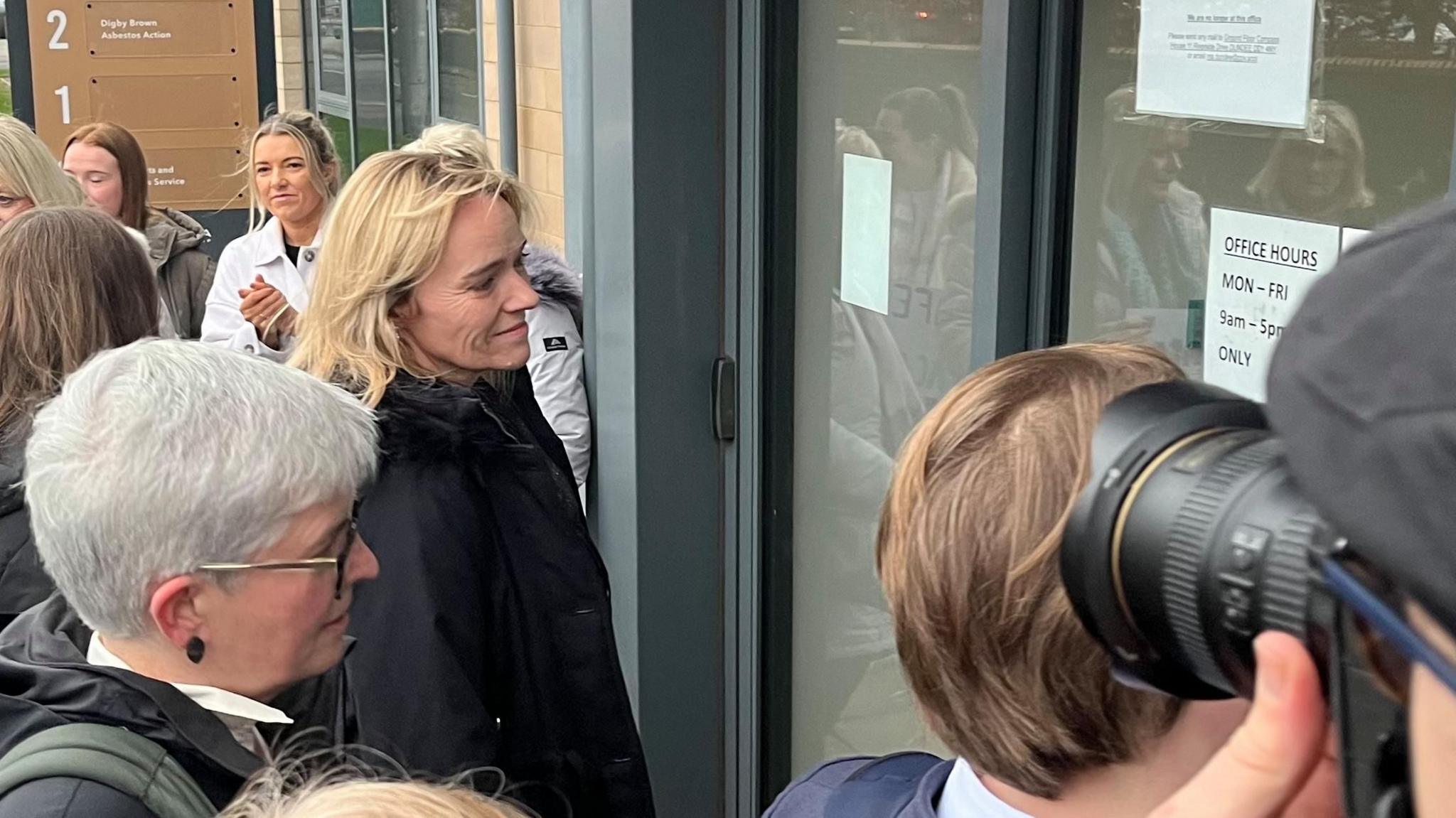 Sandie Peggie walking into the tribunal building. There are a number of other women standing in the background and beside her, and a man is holding a camera to the right of the picture.