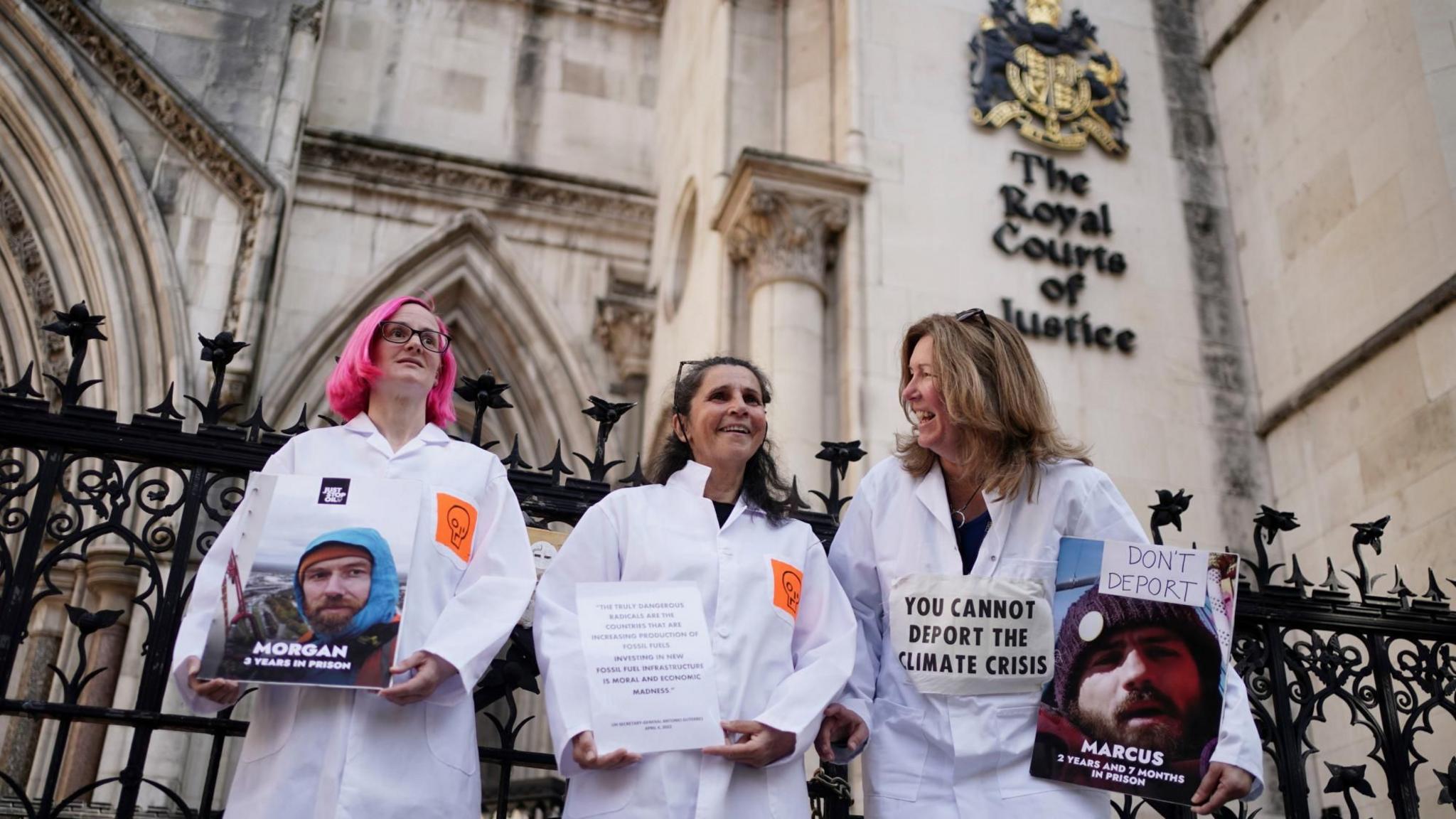 Protesters standing outside court carrying placards with faces of two jailed protesters