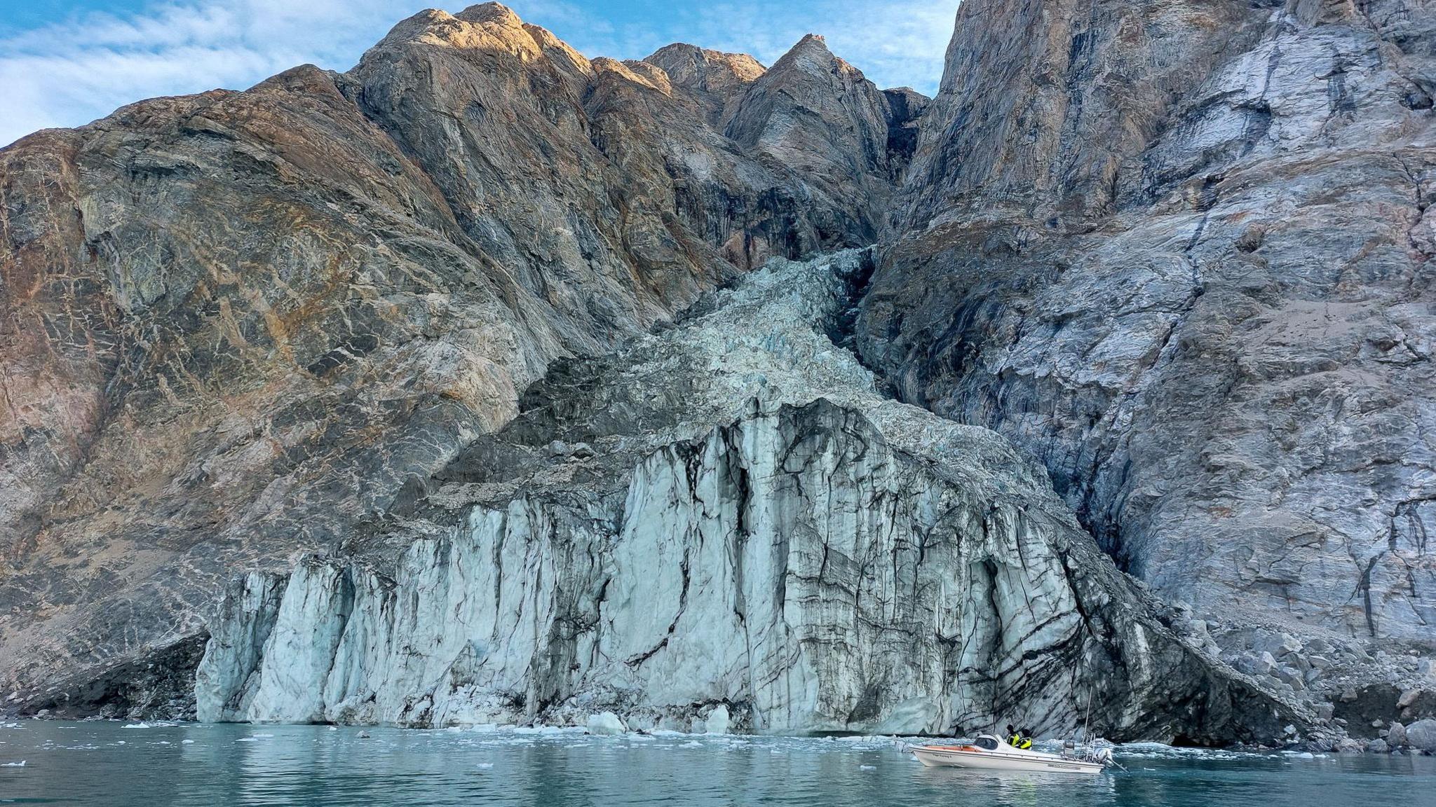 A small research boat in front of a glacier in a fjord in Greenland 