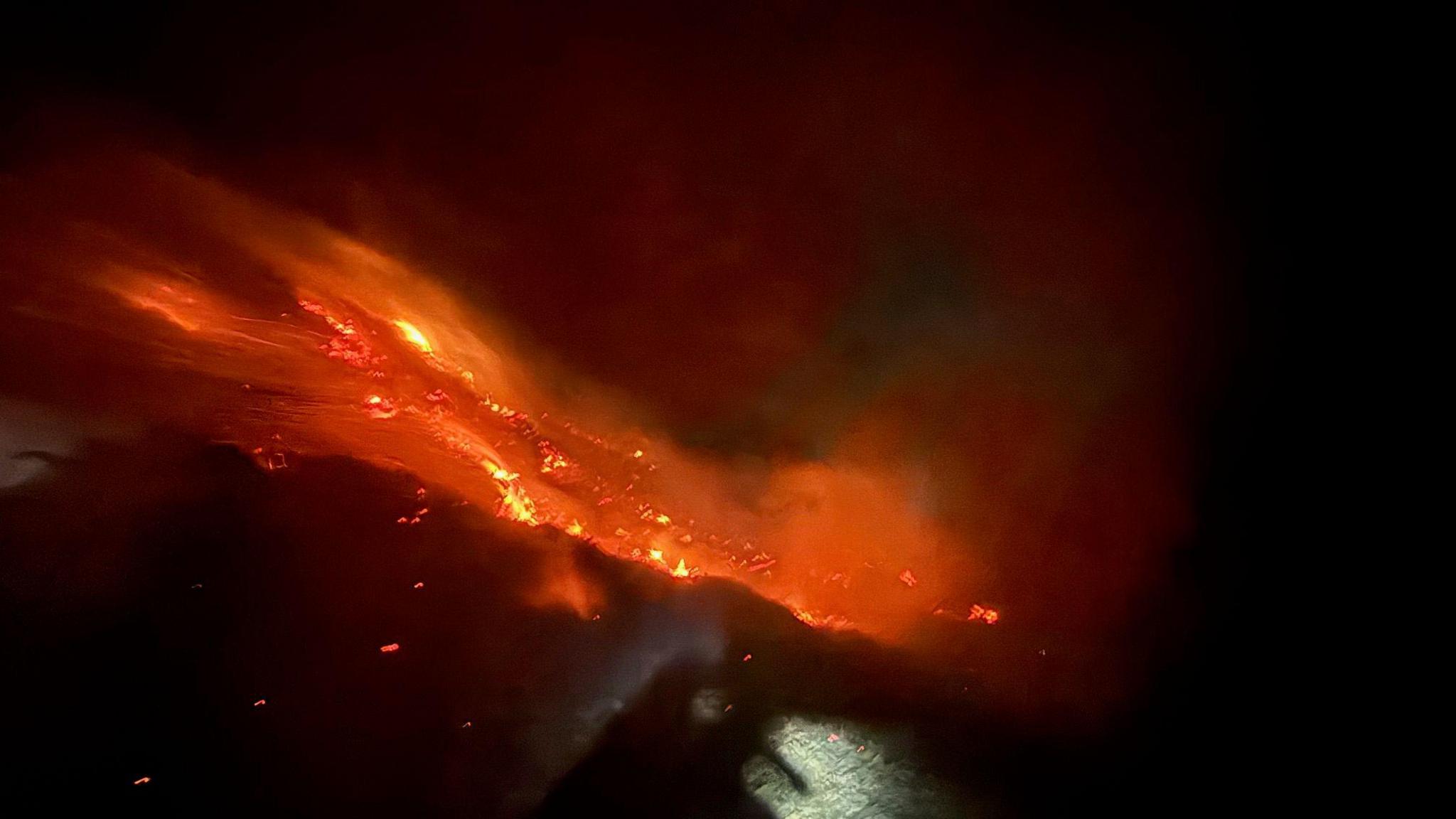 An orange glowing fire on a cliff side in Sark. Orange embers light up the black sky.