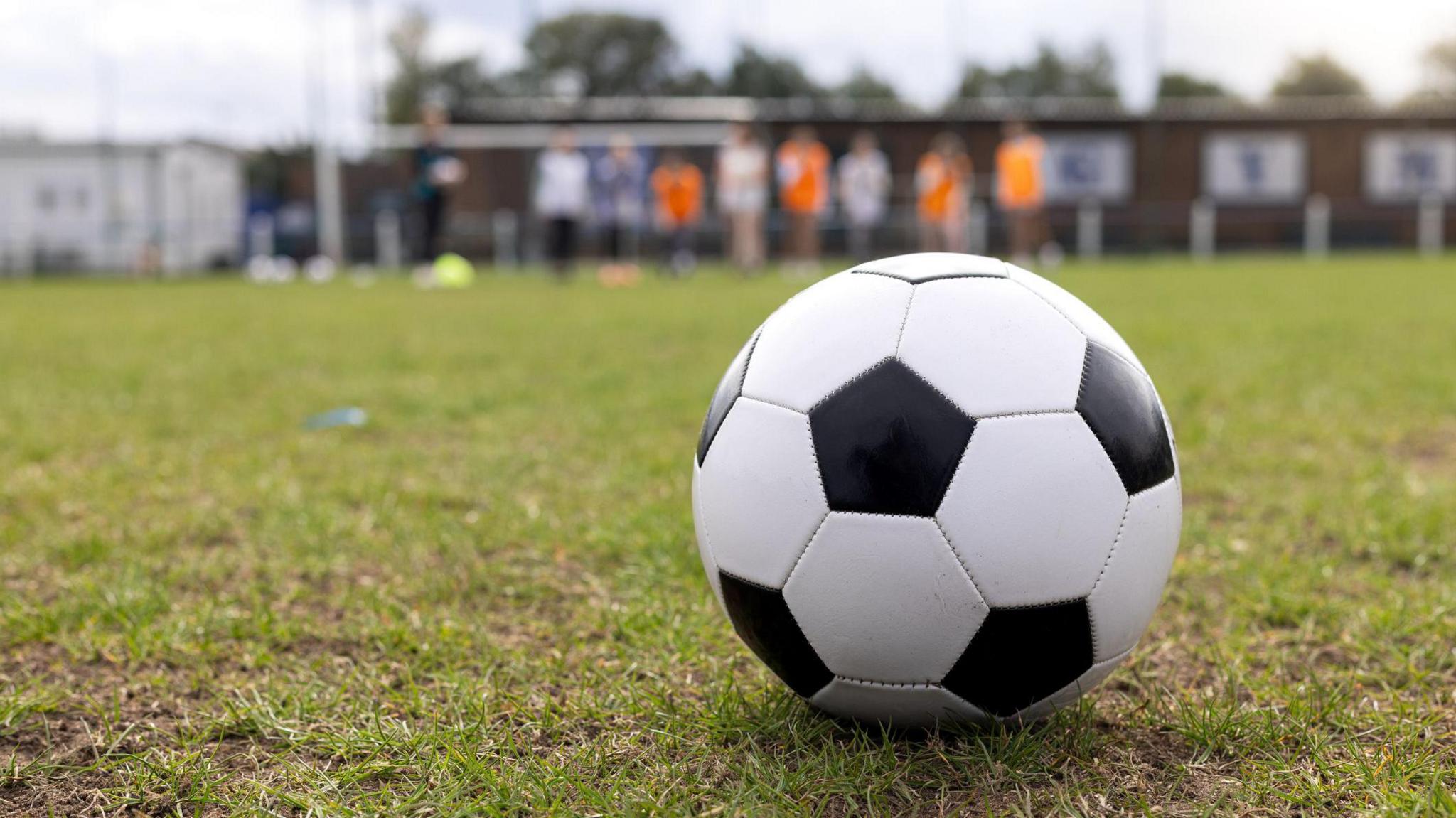 A football on a pitch with players in the background. 
