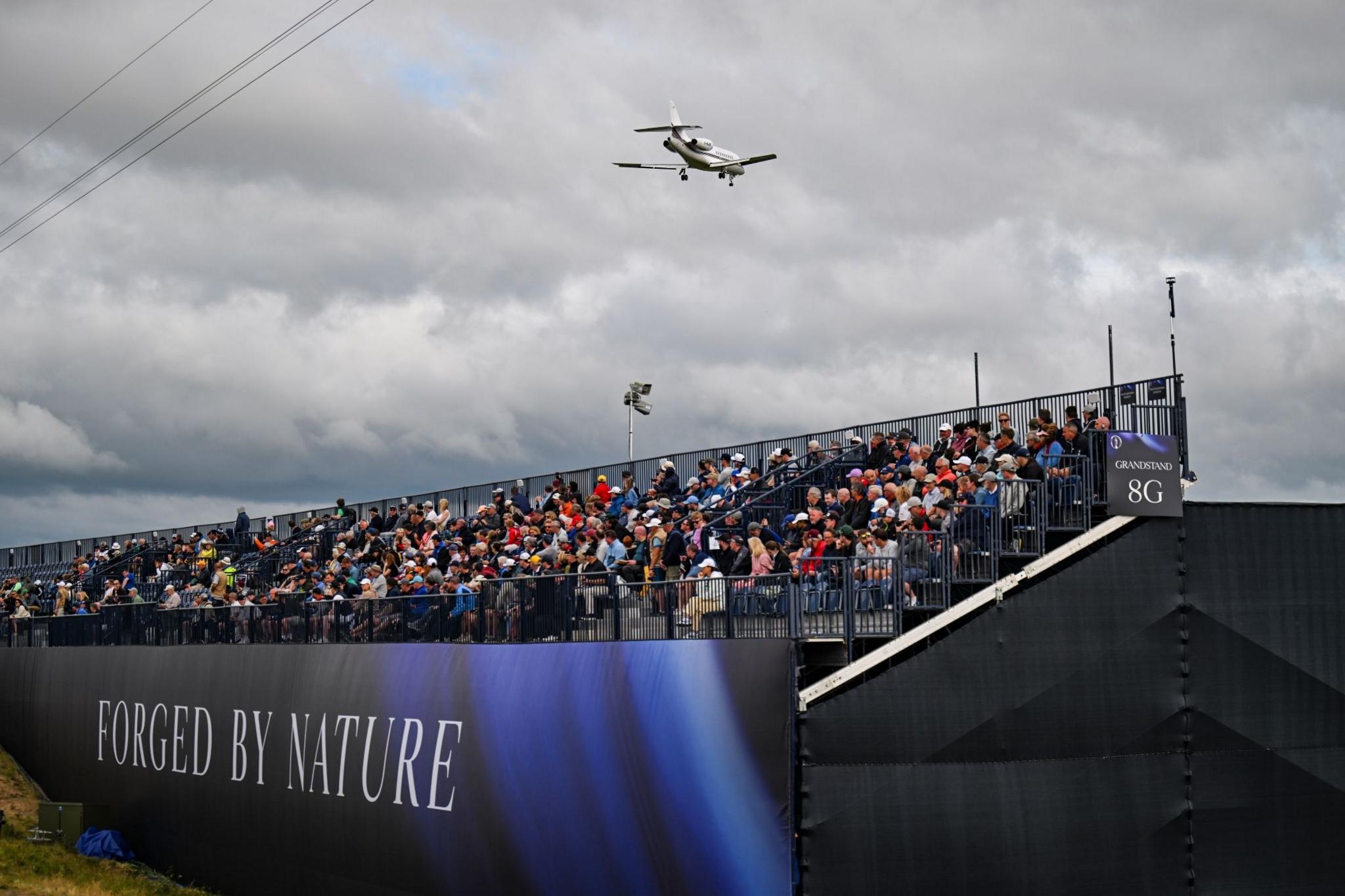 Spectators at Royal Troon Golf Club watch the action at the open as a plane approaches Glasgow Prestwick airport