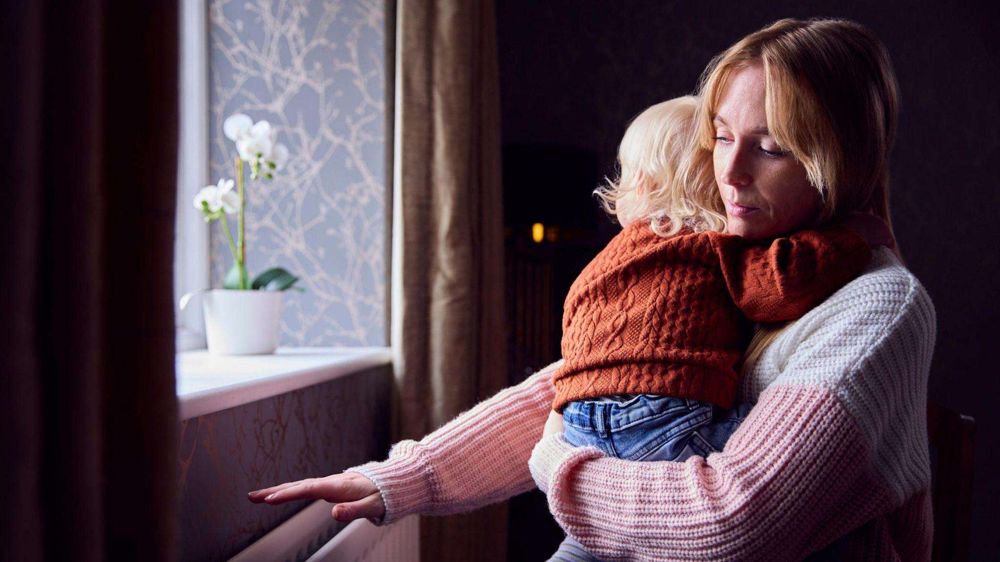 A Mother With Son Trying To Keep Warm By a Radiator At Home - stock photo