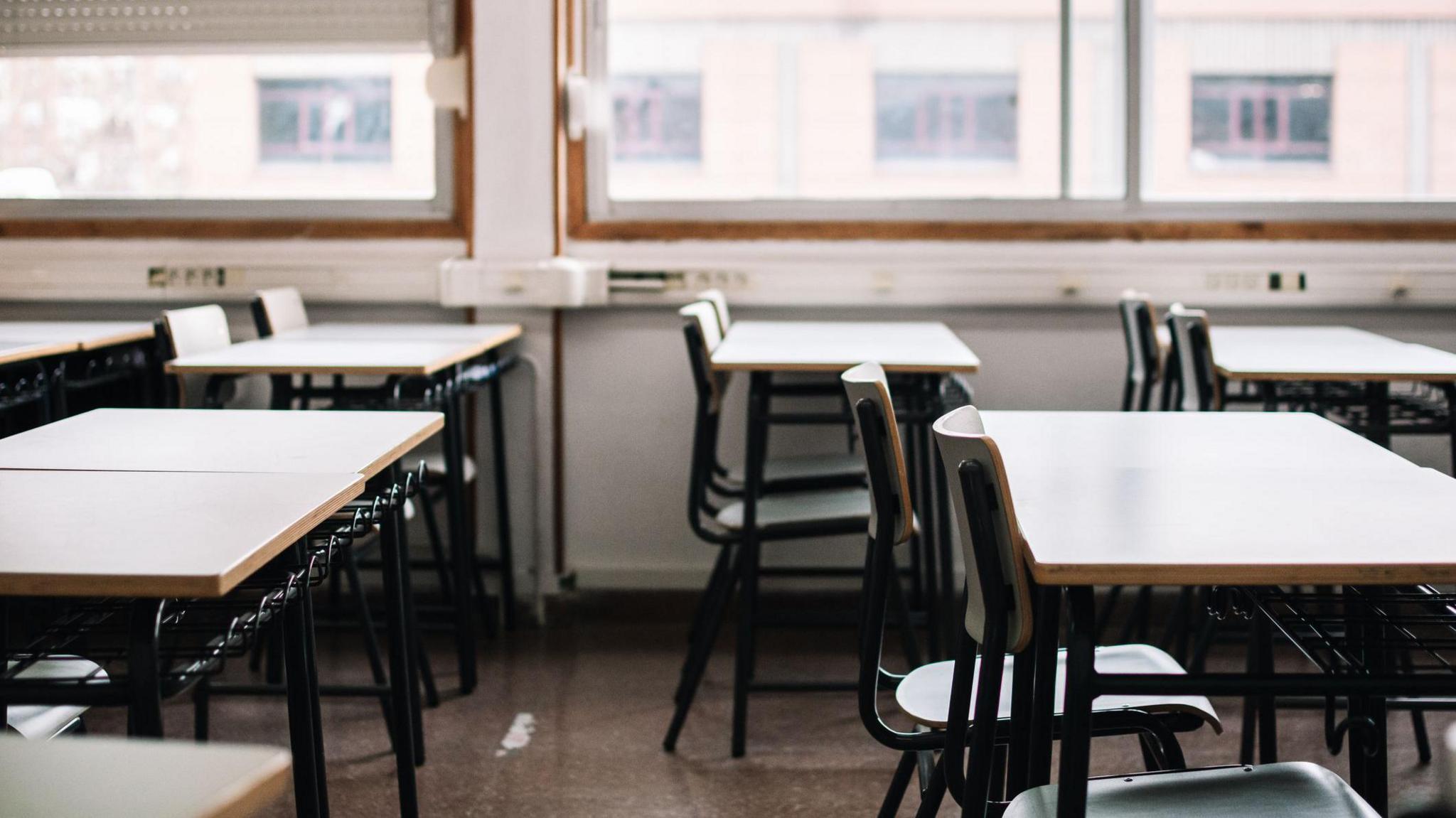 Interior of an empty classroom showing tables and chairs and a window in the background 