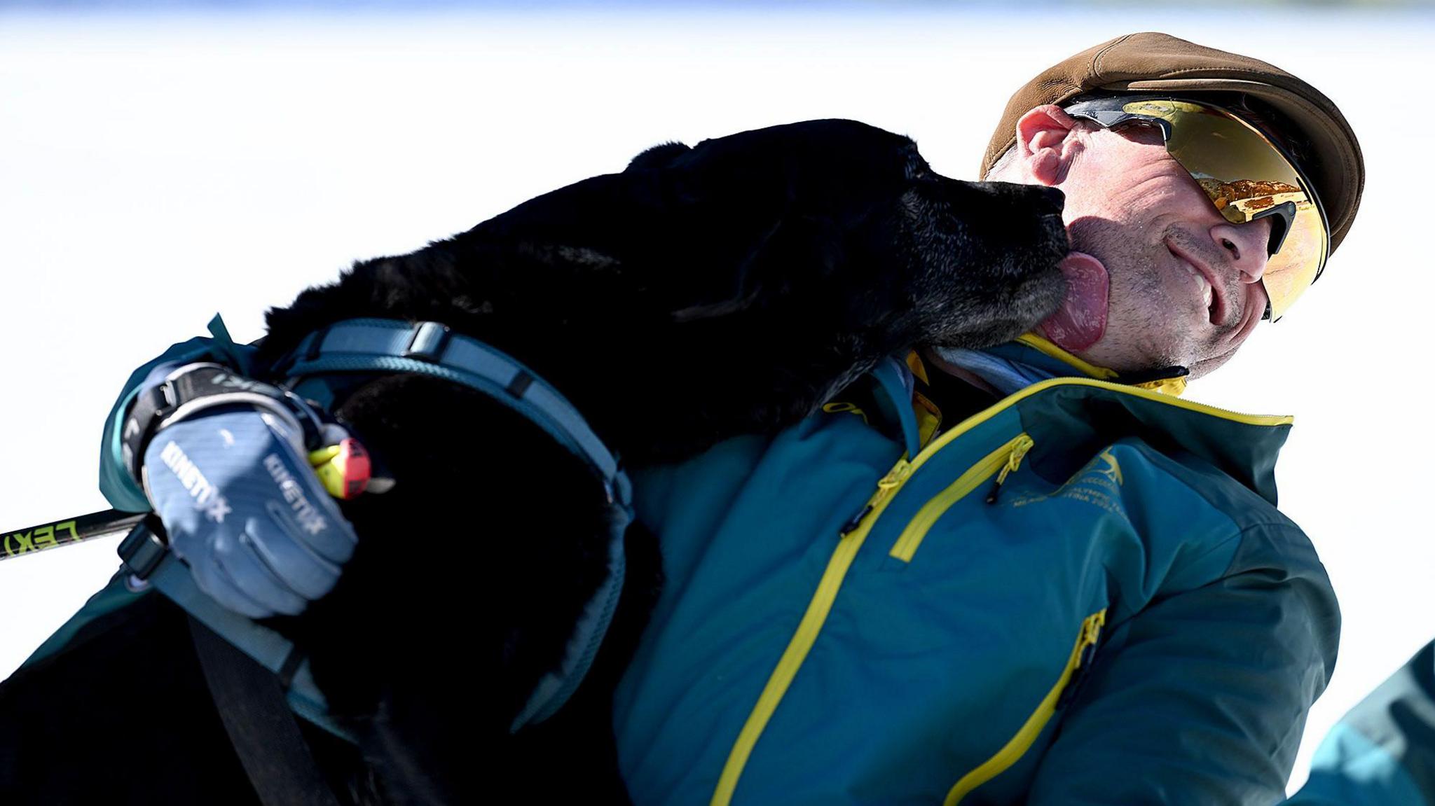 A black dog named Willow licks the face of his owner Matt Brumby on the ski slopes.