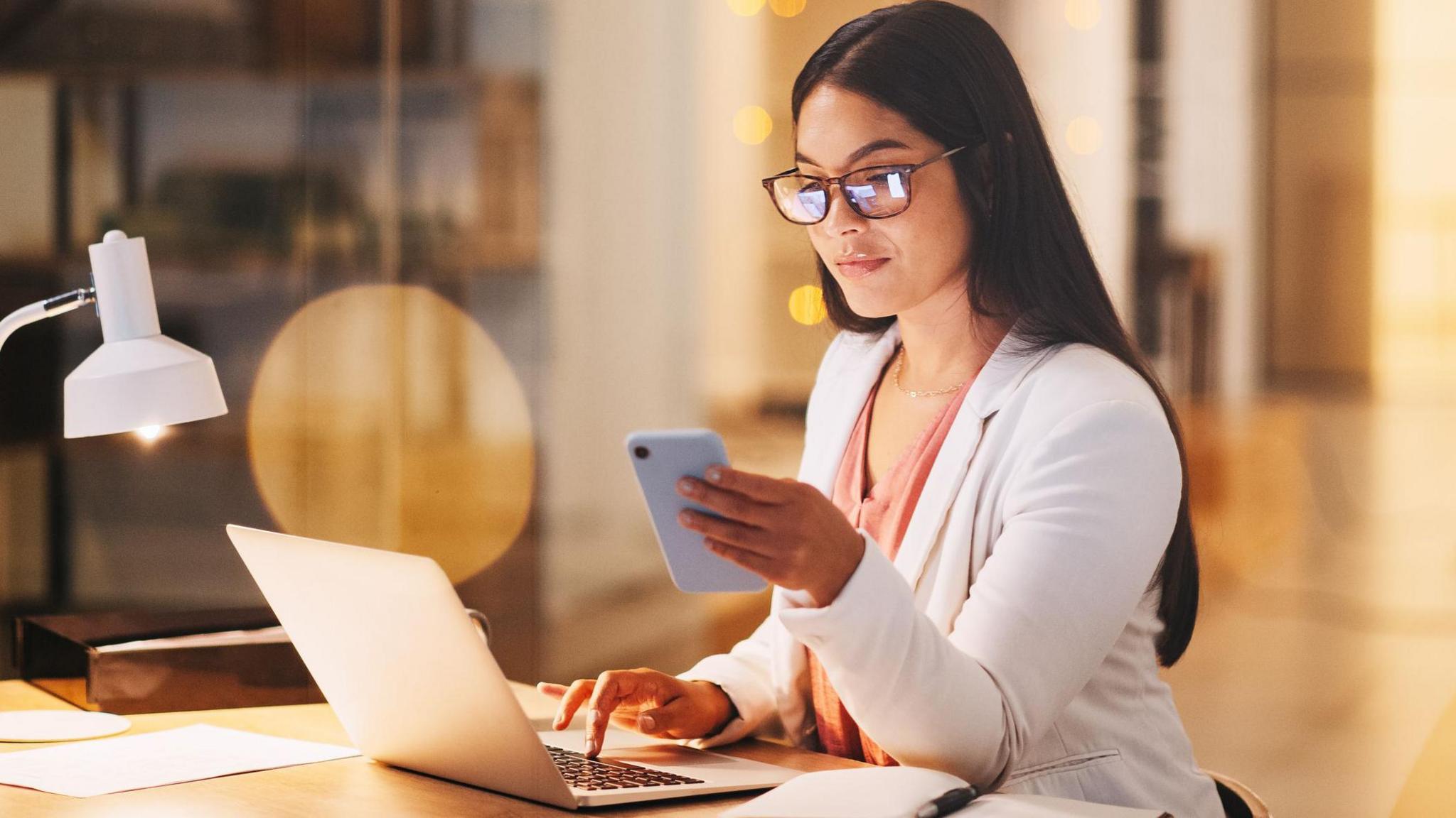 A woman sitting at her computer and using her phone