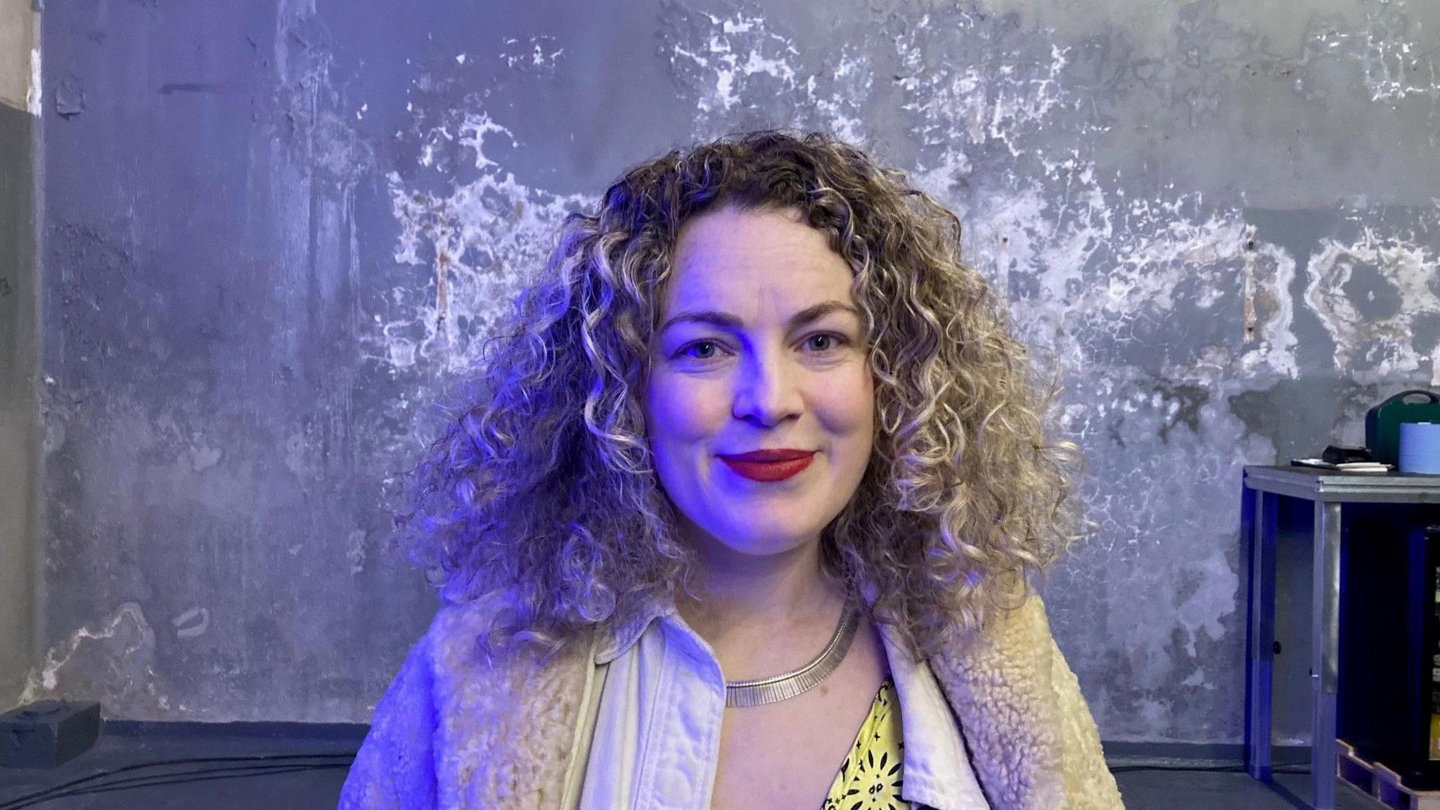 A woman with curly hair and a white fleece coat and shirt. 