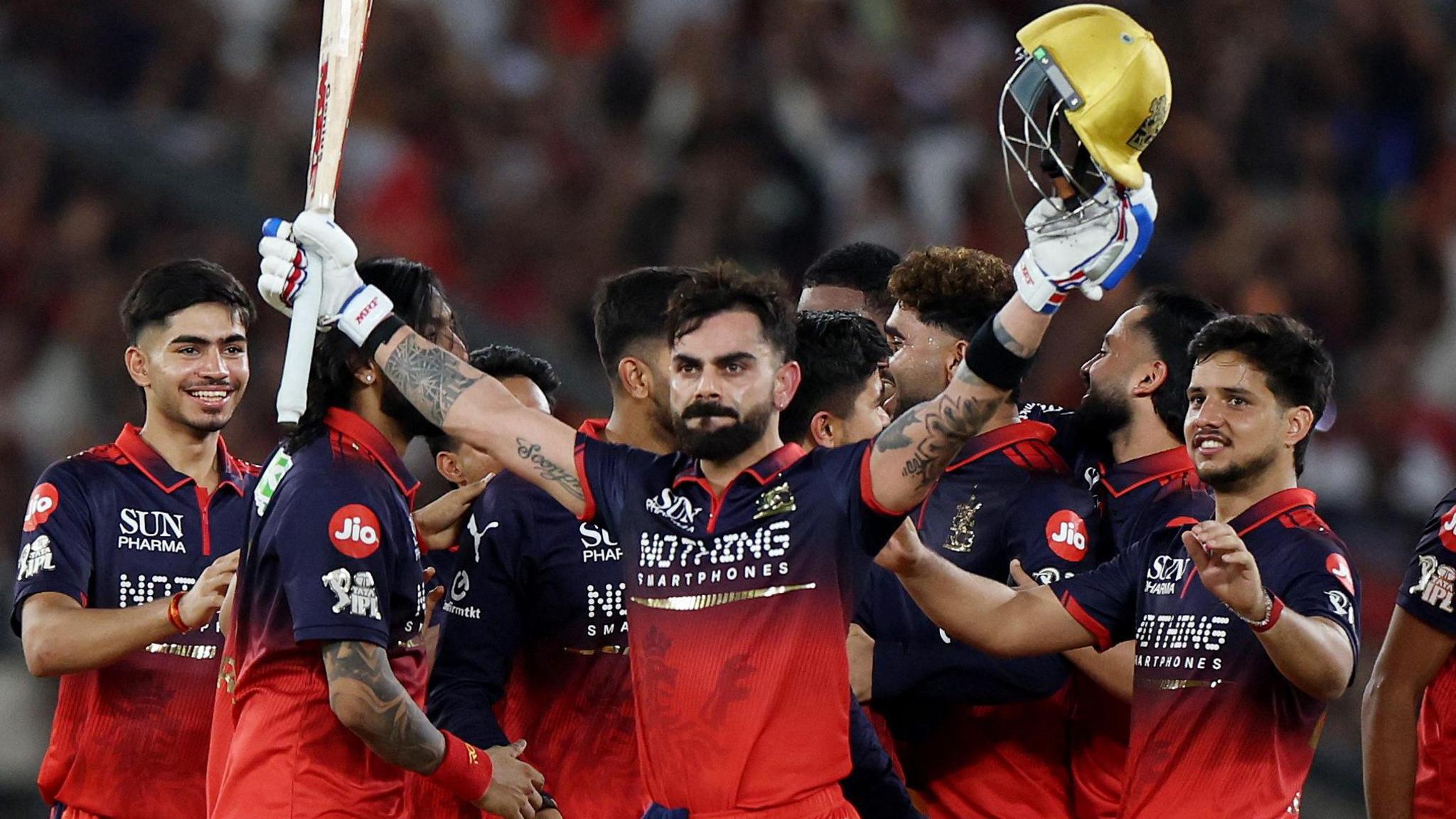 Virat Kohli holds his bat and helmet aloft as his RCB team-mates celebrate winning the IPL
