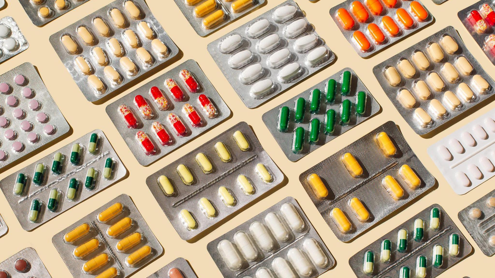 A selection of blister packs of medication, including white pills, yellow pills, green and white pills and orange pills 