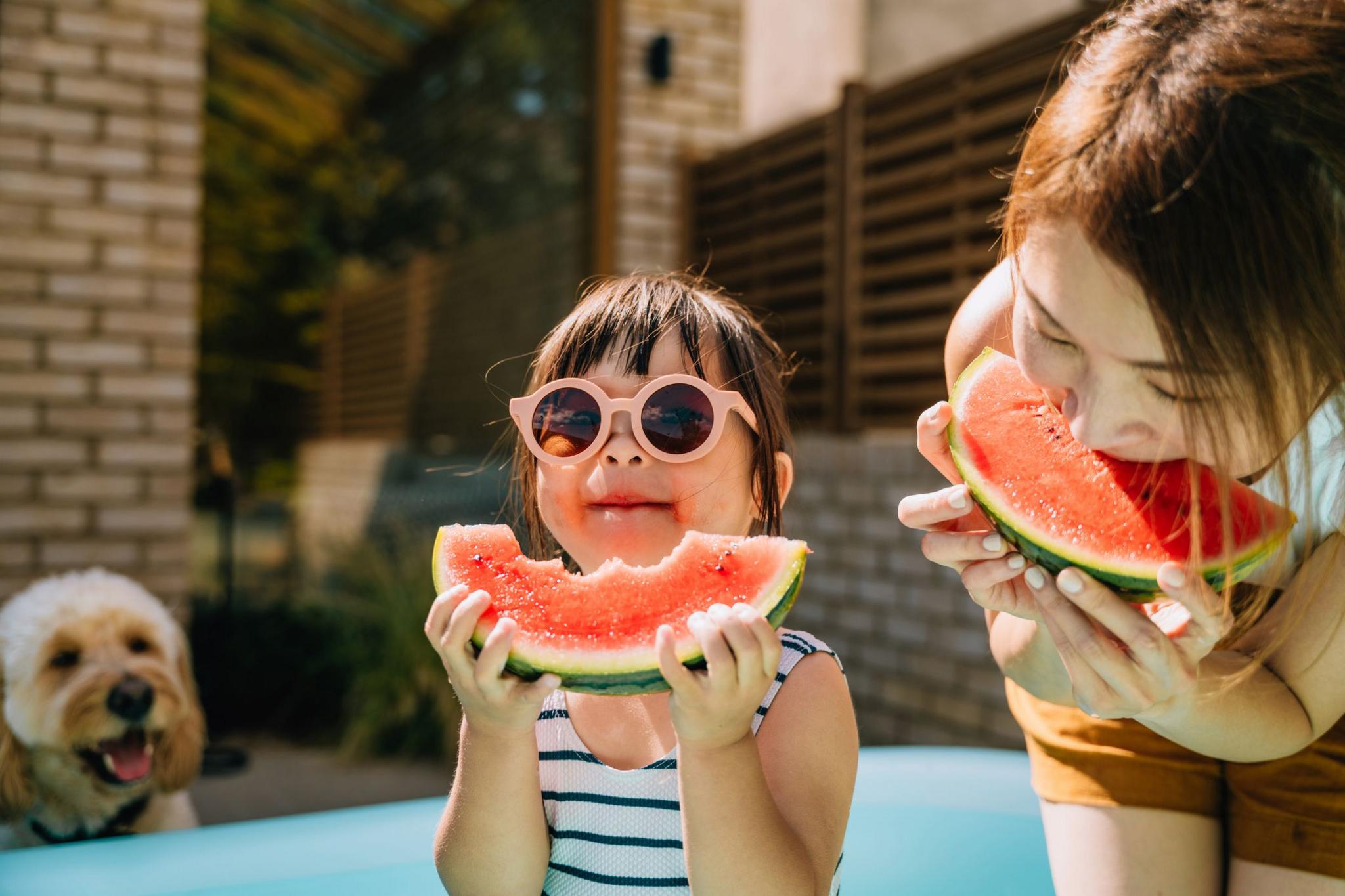 Asian little girl with sunglasses, enjoying summertime, eating fresh ripe watermelon with her mother.