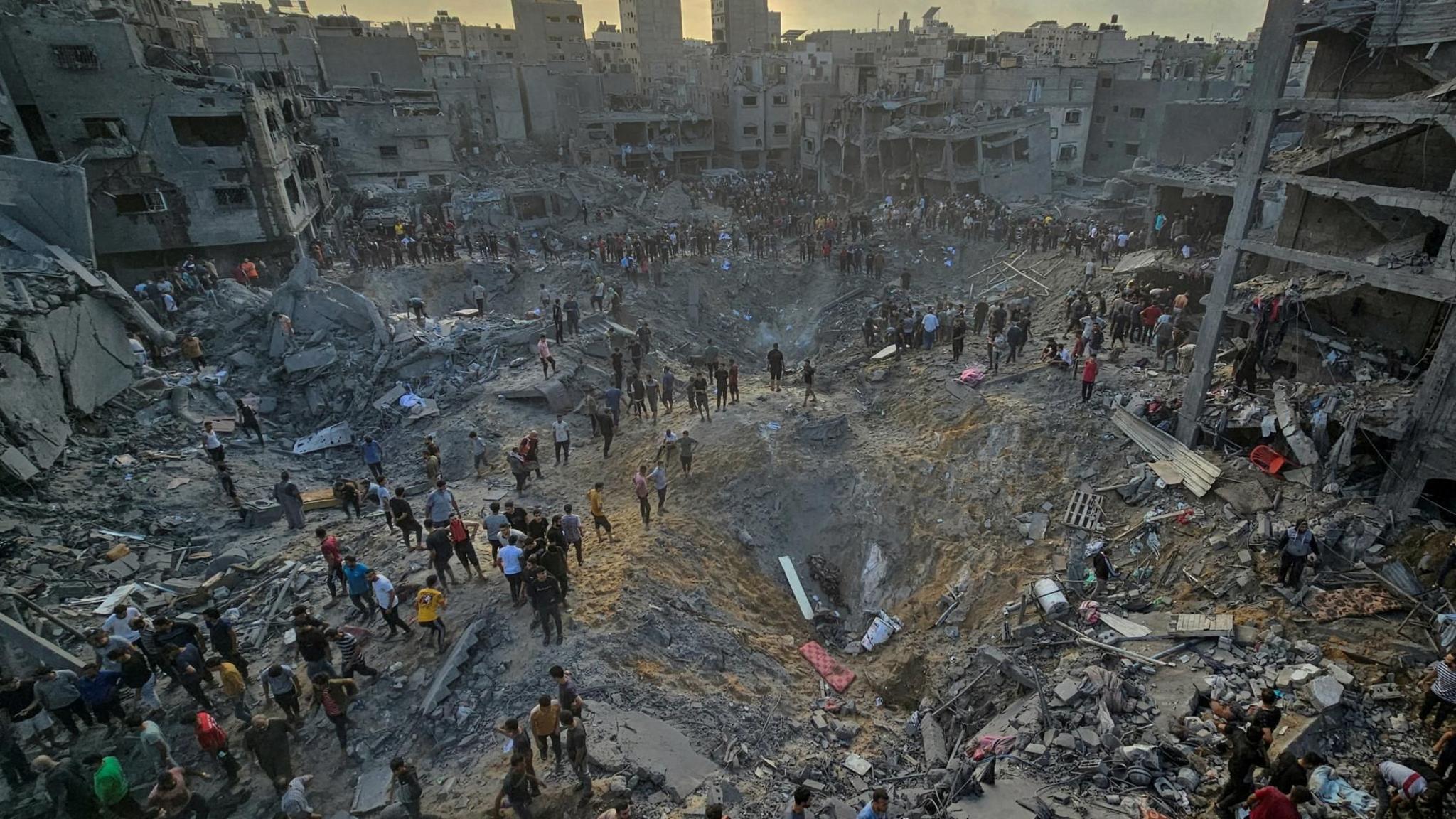 Palestinians walk past large craters and the rubble of destroyed buildings in Jabalia refugee camp, in the northern Gaza Strip (31 October 2023)