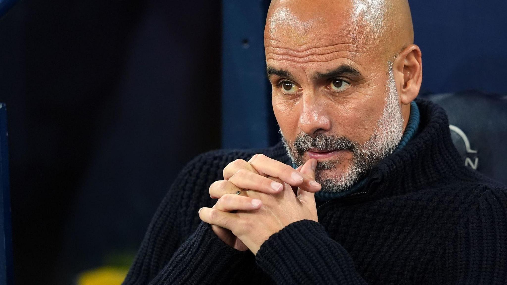 Pep Guardiola sits in the Manchester City dugout