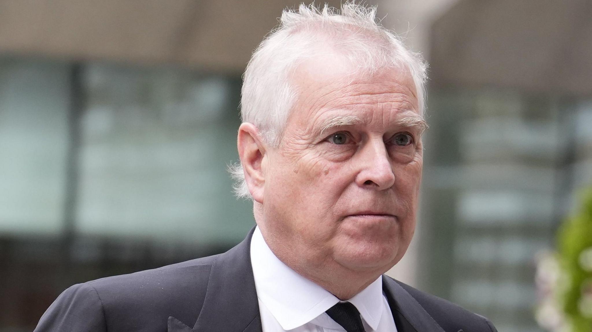 Andrew Mountbatten Windsor has grey hair. He is looking to the right. You can see the top of a suit and black tie.