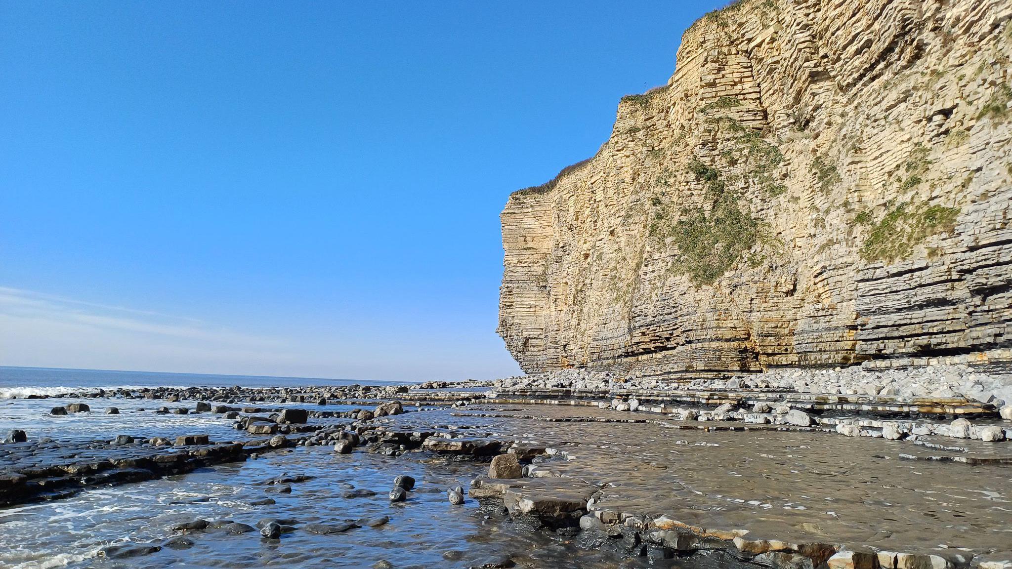a tall  limestone cliff above the sea on a blue sky day