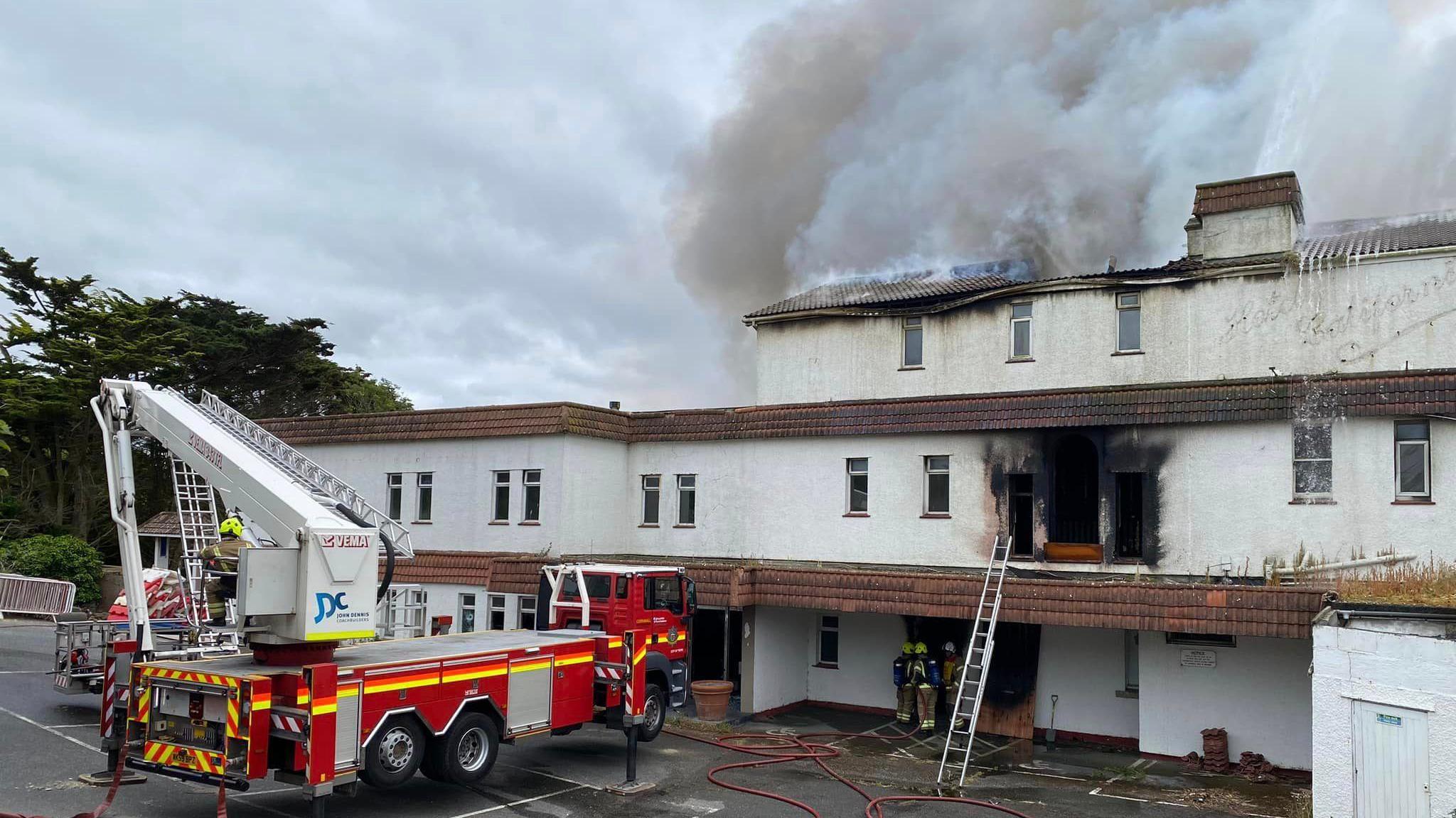 A fire engine and fire crew in front of the burning hotel